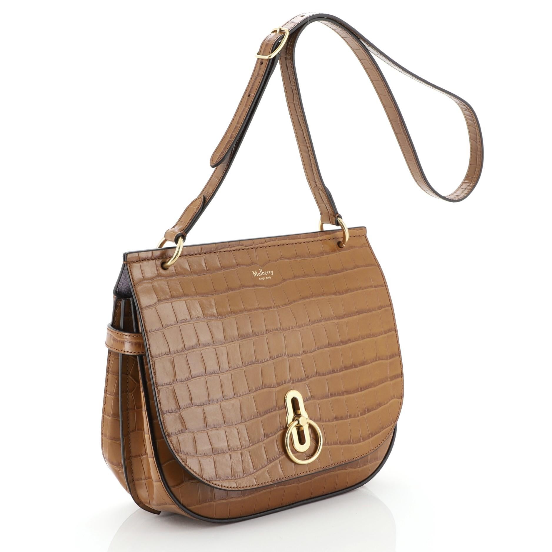 This Mulberry Amberley Crossbody Bag Crocodile Embossed Leather Medium, crafted in brown crocodile-embossed leather, features an adjustable shoulder strap, and matte gold-tone hardware. Its turn-lock closure opens to a purple suede