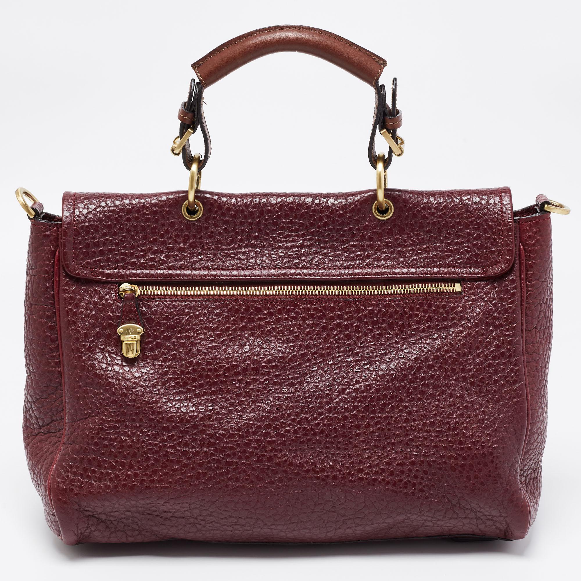 This Mulberry top handle bag will instantly elevate any outfit with its classic burgundy color and gold-tone hardware. It is crafted from grained leather and has a structured shape. The smooth fabric-suede interior has ample room for your