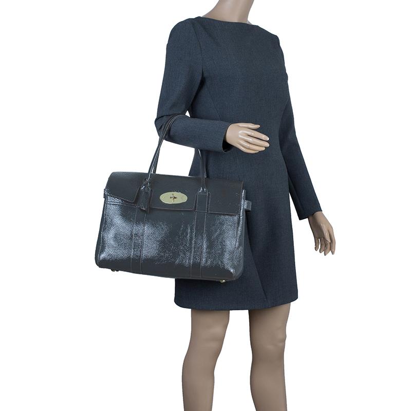 This celebrity coveted Bayswater handbag by Mulberry is timeless. This version is crafted from a dark hued grey patent leather that features the well known Postman’s lock closure in gold-tone hardware, rolled leather handles and a leather tag. The