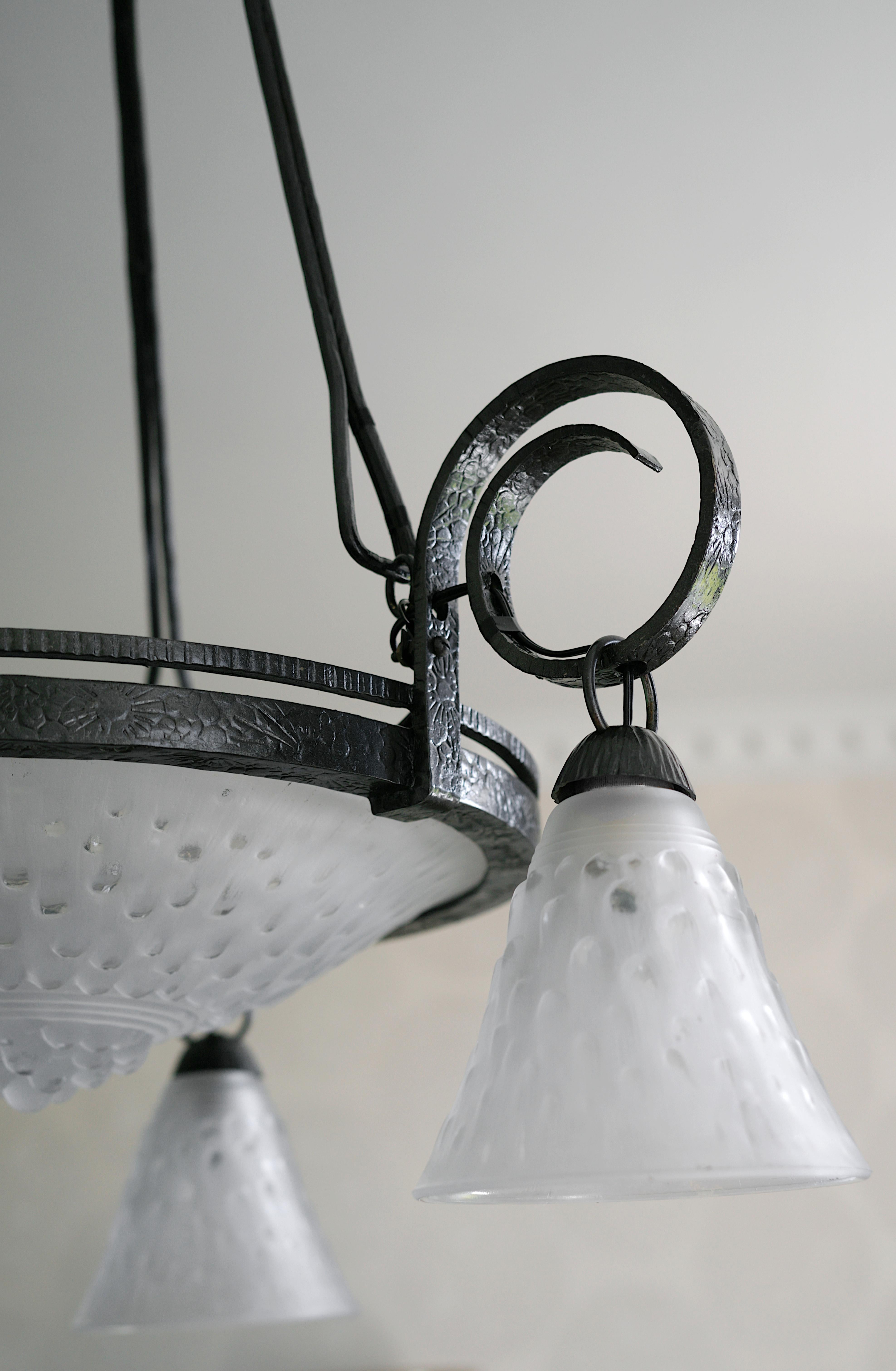 Lampadario francese Art Déco di MULLER FRERES (Luneville), Francia, 1920 circa. Questo splendido lampadario è caratterizzato da spessi paralumi in vetro smerigliato sospesi da un apparecchio in ferro battuto nell'iconico modello 