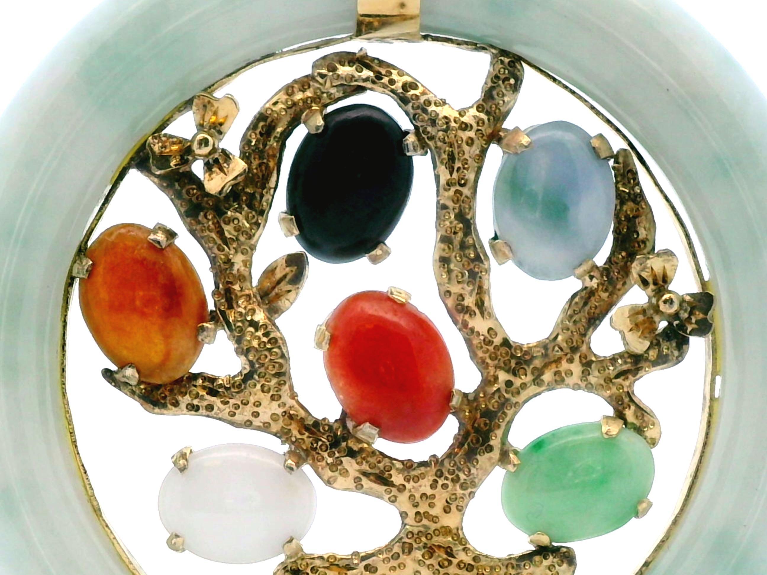 This stunning pendant is made from mixed colors of jade as well as 14k yellow gold. The border is made from a hololith mottled green jade that showcases the design inside. It features a 14k yellow gold tree with mixed colors of cabochon jade spread