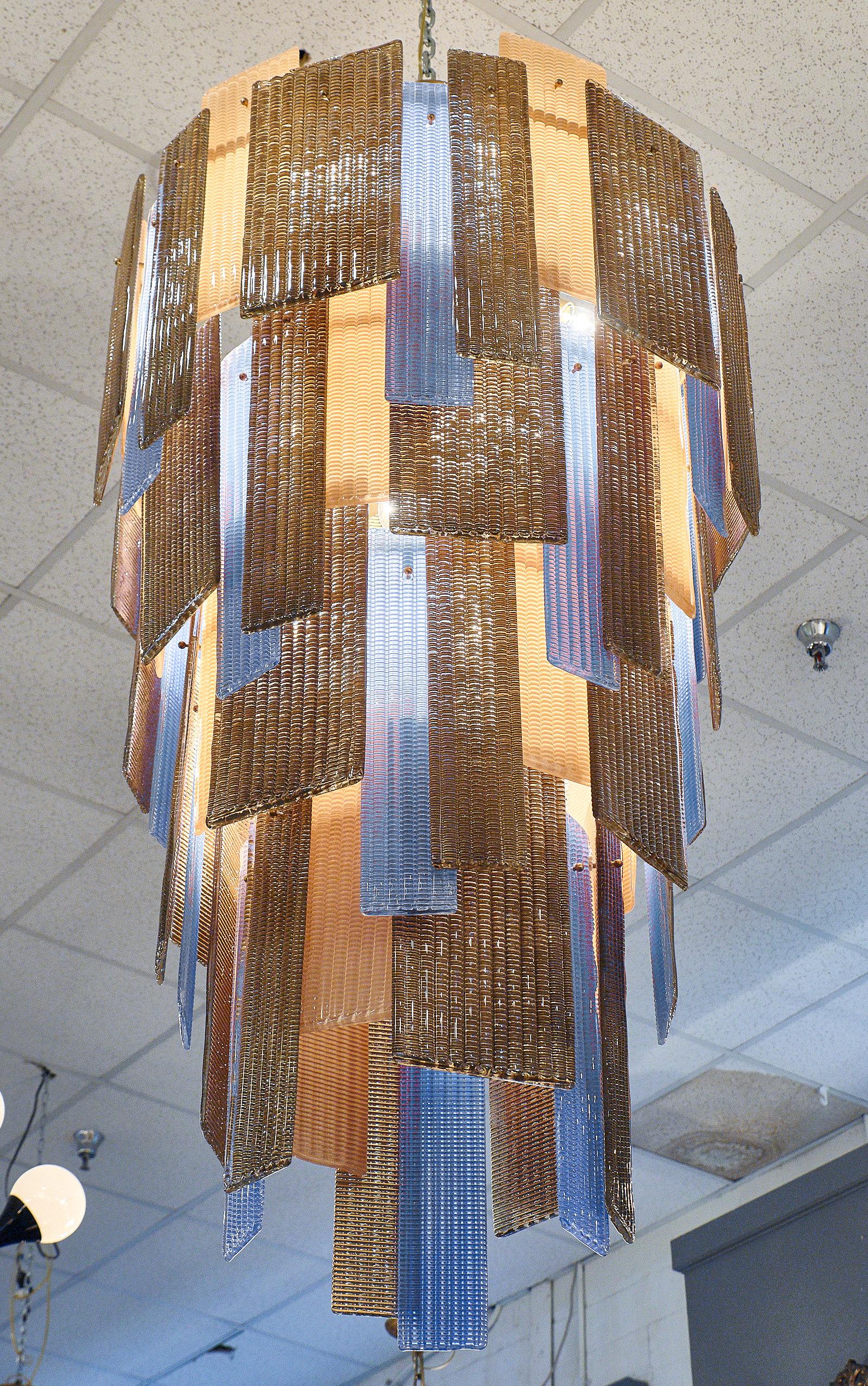 Murano ridged glass multi-color chandelier in periwinkle, bronze, and light peach. The four cascading tiers have alternating color and size glass plates to create a dynamic and unique design. The fixture requires twelve medium-base bulbs up to 60