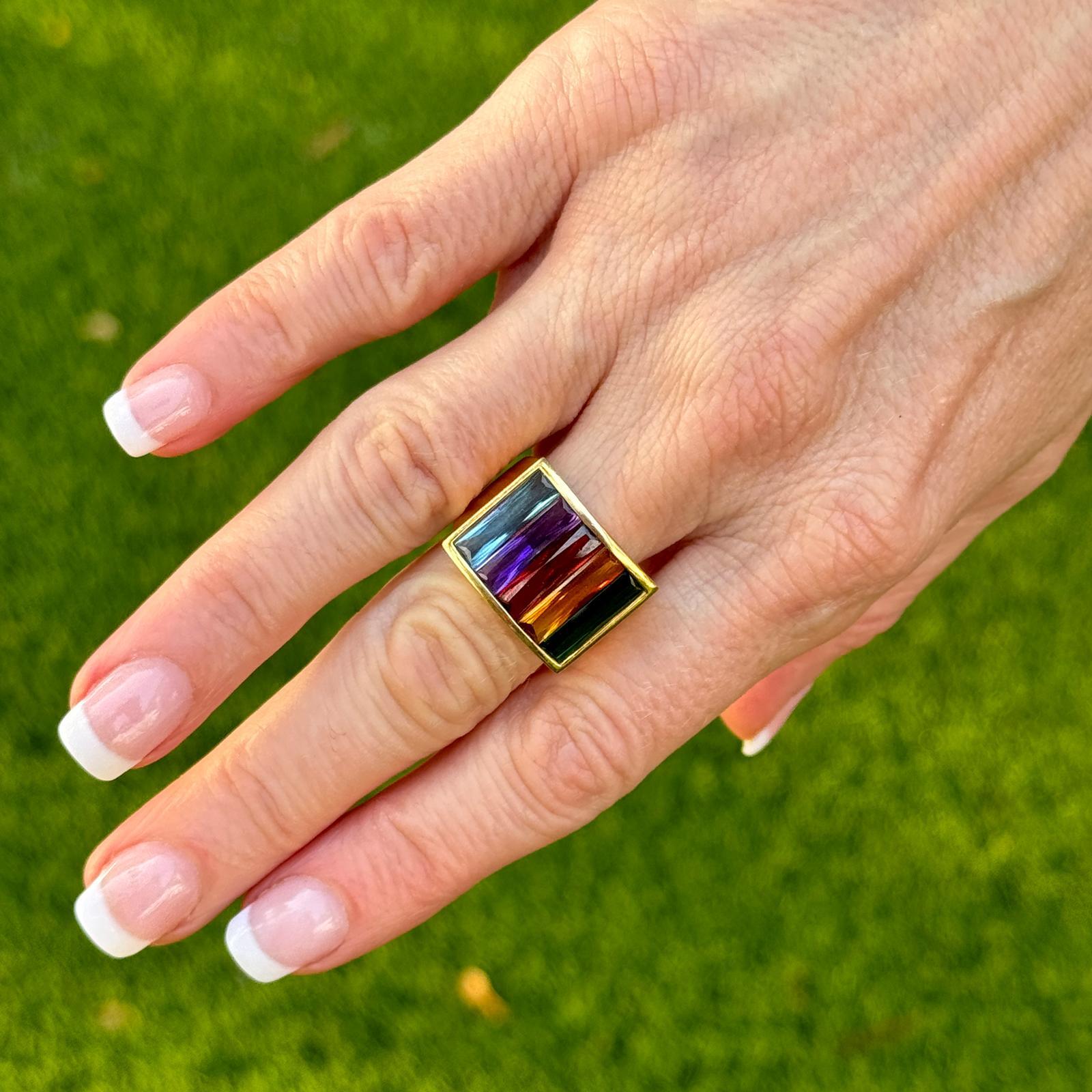 Multi-Color gemstone vintage band ring crafted in 18 karat yellow gold. The band features baguette cut multi-color tourmaline, citrine, and amethyst gemstones in a rainbow design. The ring measures 15 x 20mm on top and is currently size 7 (can be