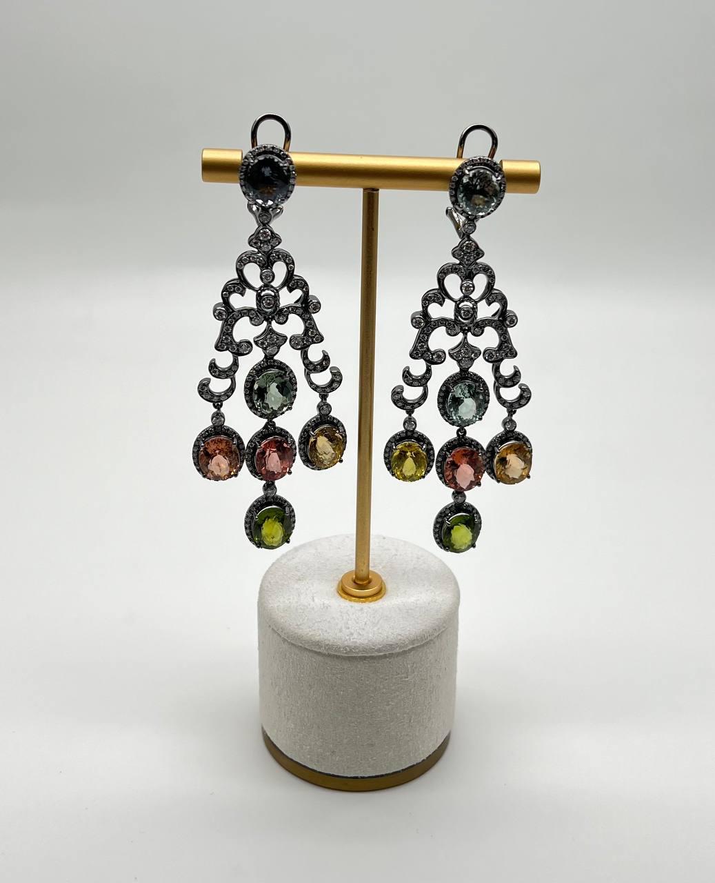 Crafted with intricate metalwork, these earrings feature a cascading design adorned with multicolored tourmalines. The gemstones are set in ornate, openwork patterns, creating a dynamic and eye-catching movement. Each earring showcases a harmonious