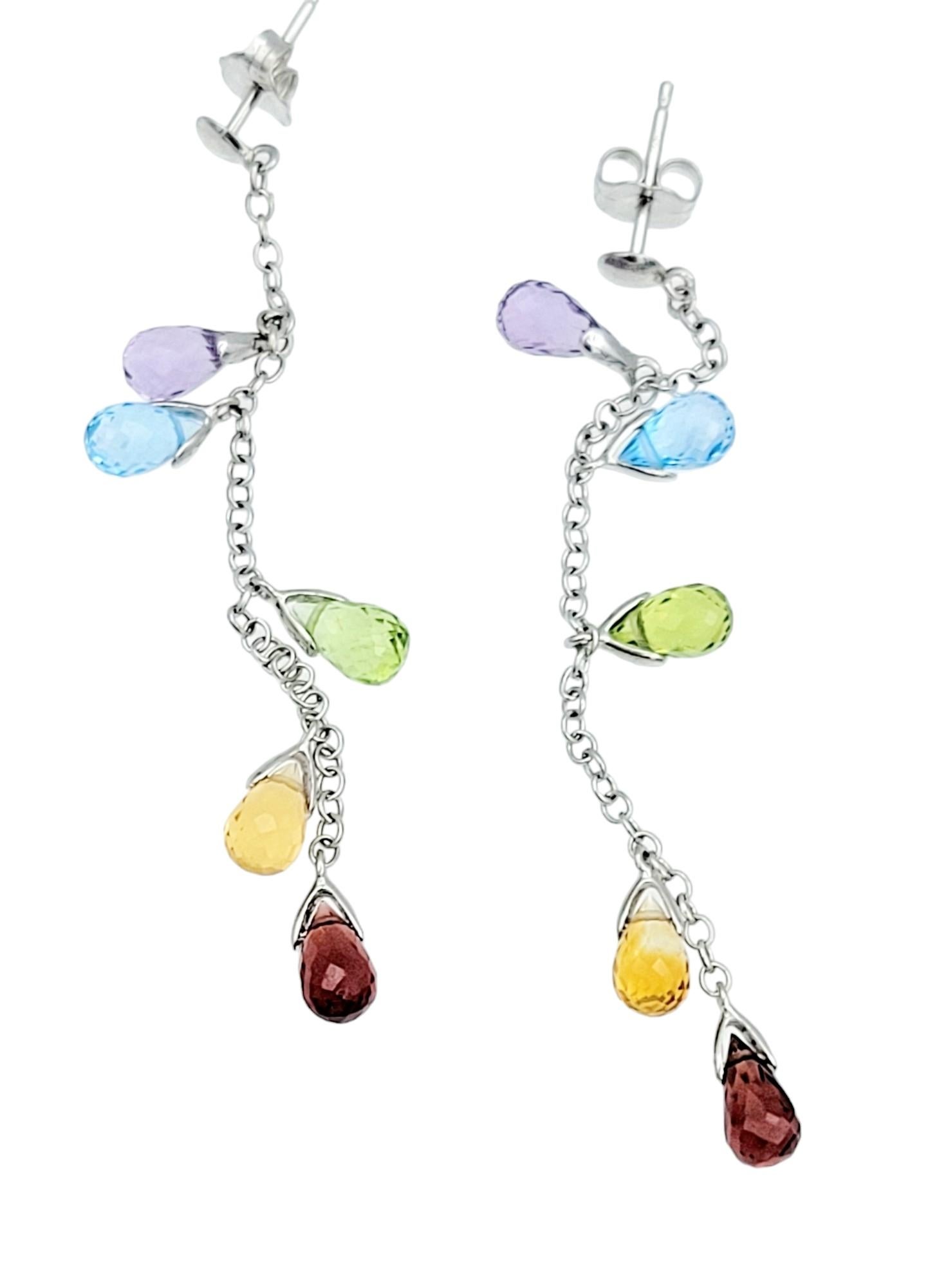 These exquisite dangle earrings, set in radiant 14 karat white gold, boast a vibrant and playful design. The earrings feature a delicate cable chain adorned with briolette-cut gemstones that dangle gracefully in a rainbow order. The sequence of