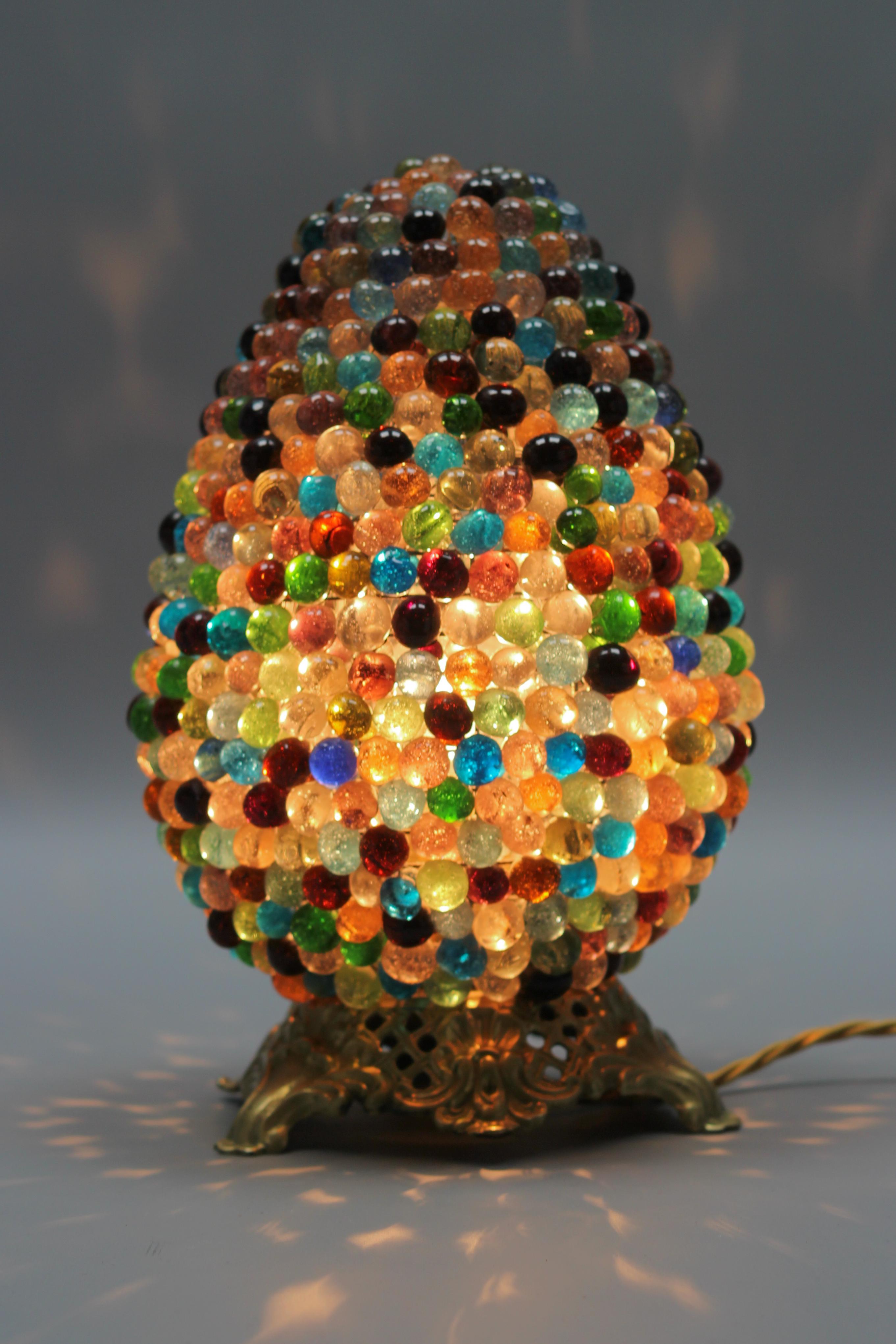 A superb Murano glass and bronze table lamp. The oviform-shaped lamp shade features multicolored round glass beads. The beautiful glass lampshade is mounted on a Rococo-style bronze base.
The single socket holds an E27 (E26) base bulb. 
To the US