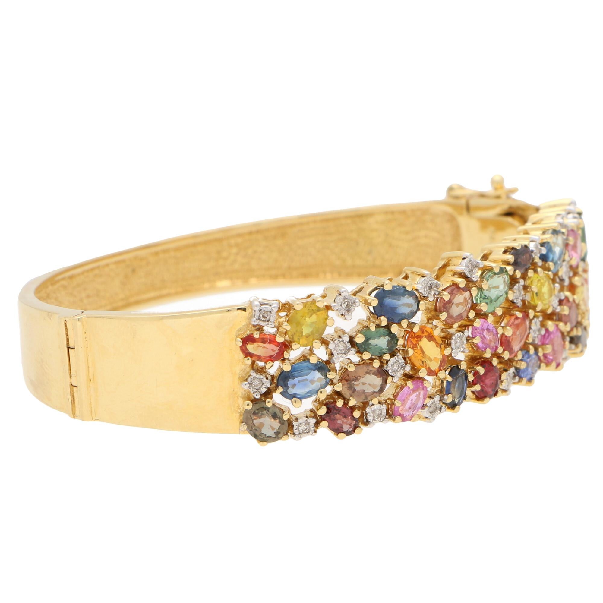 An extremely unique multi-colored sapphire and diamond wide cuff bangle bracelet set in 18k yellow gold.

This colorful piece is claw set with a panel of various colored sapphires which are interspersed amongst a number of sparkly round brilliant