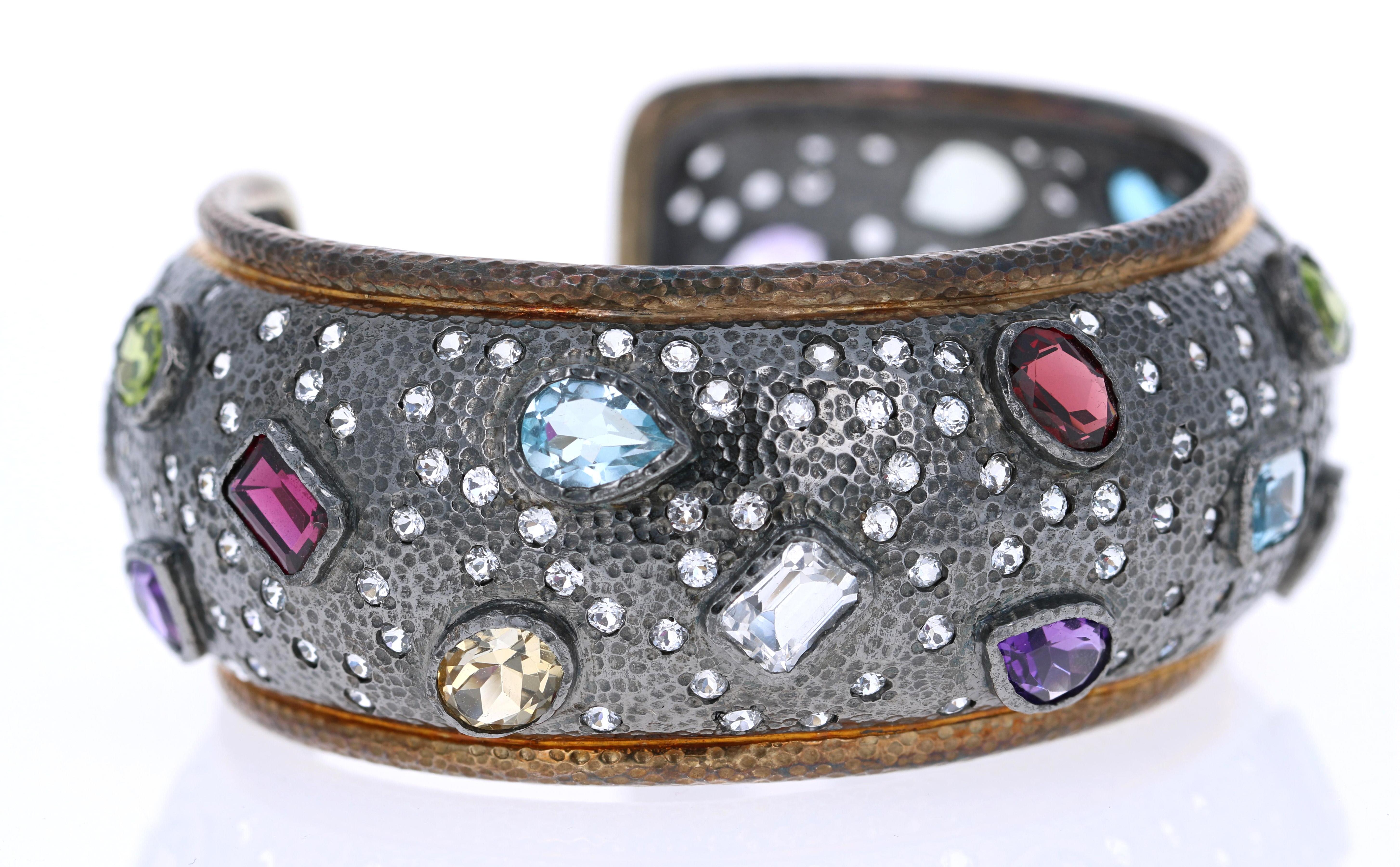This Multi Colored Stone Cuff Bangle has Oval, Pear and Emerald Cut stones that are genuine Amethysts, Blue Topaz, Garnets, Peridot, White Topaz, and Citrines. 

The bangle is handmade in 925 silver with a hammered effect on the metal. 

Dress it up