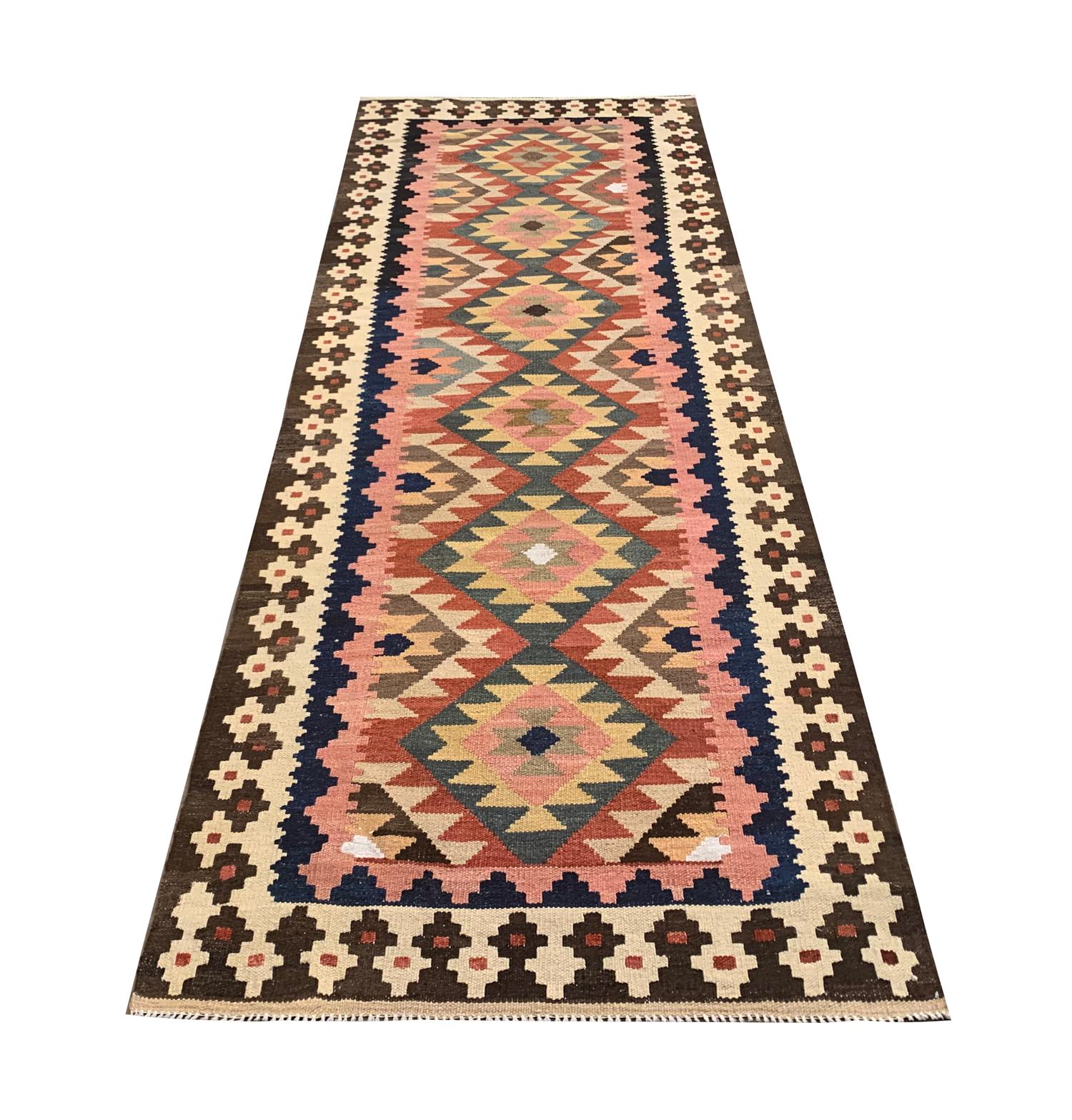 This handwoven bold wool kilim is a vintage Afghan rug woven by hand in the early 21st century, circa 2010. In this geometric rug, the central design features a bold pattern woven with beige, pink, green and beige accents. The colour palette of the