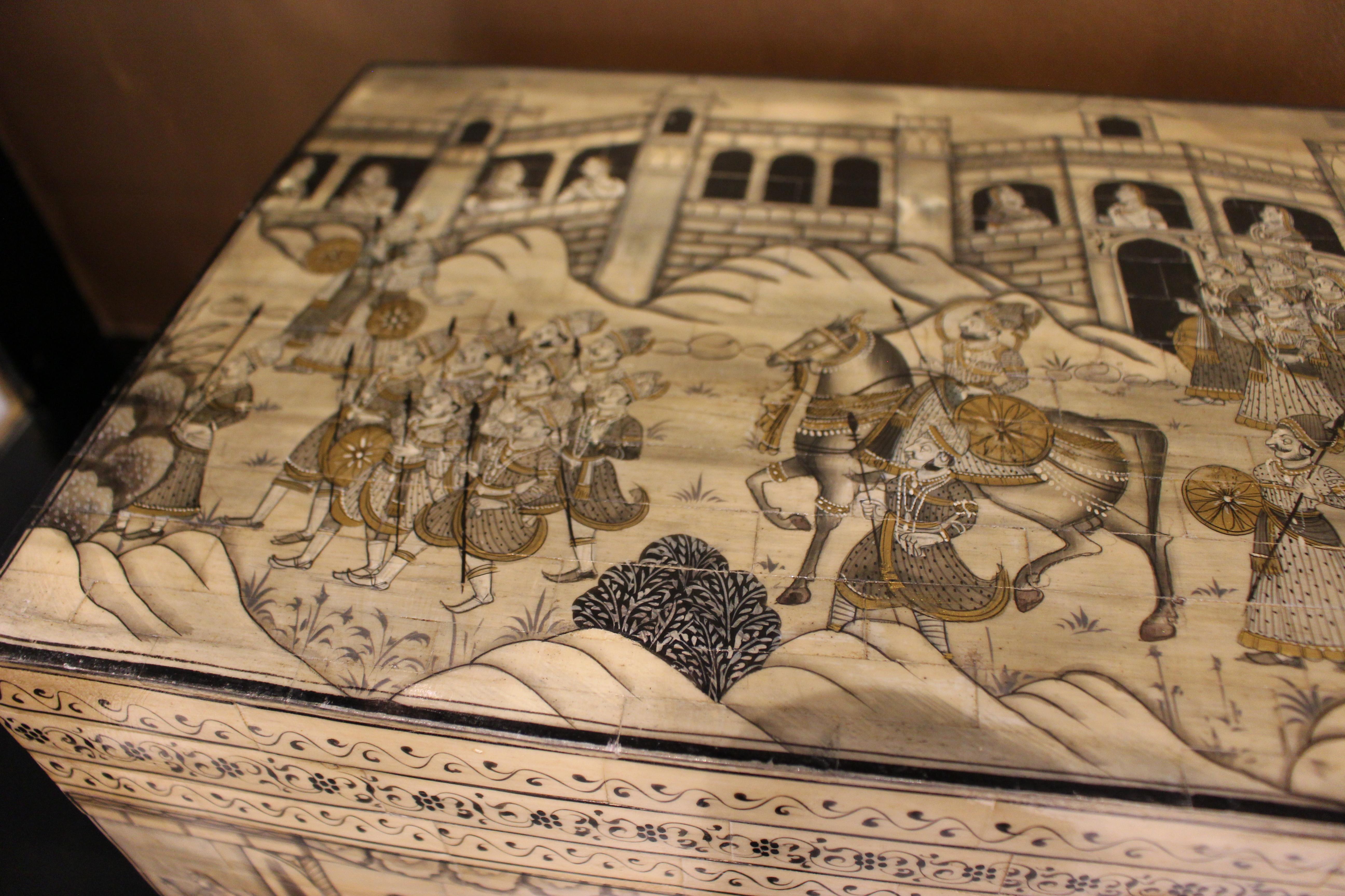 Lackierte indische Accessoirebox mit mehreren Fächern in rechteckiger Form mit seitlichen Griffen und der Darstellung einer Außenszene mit Menschen und Tieren.