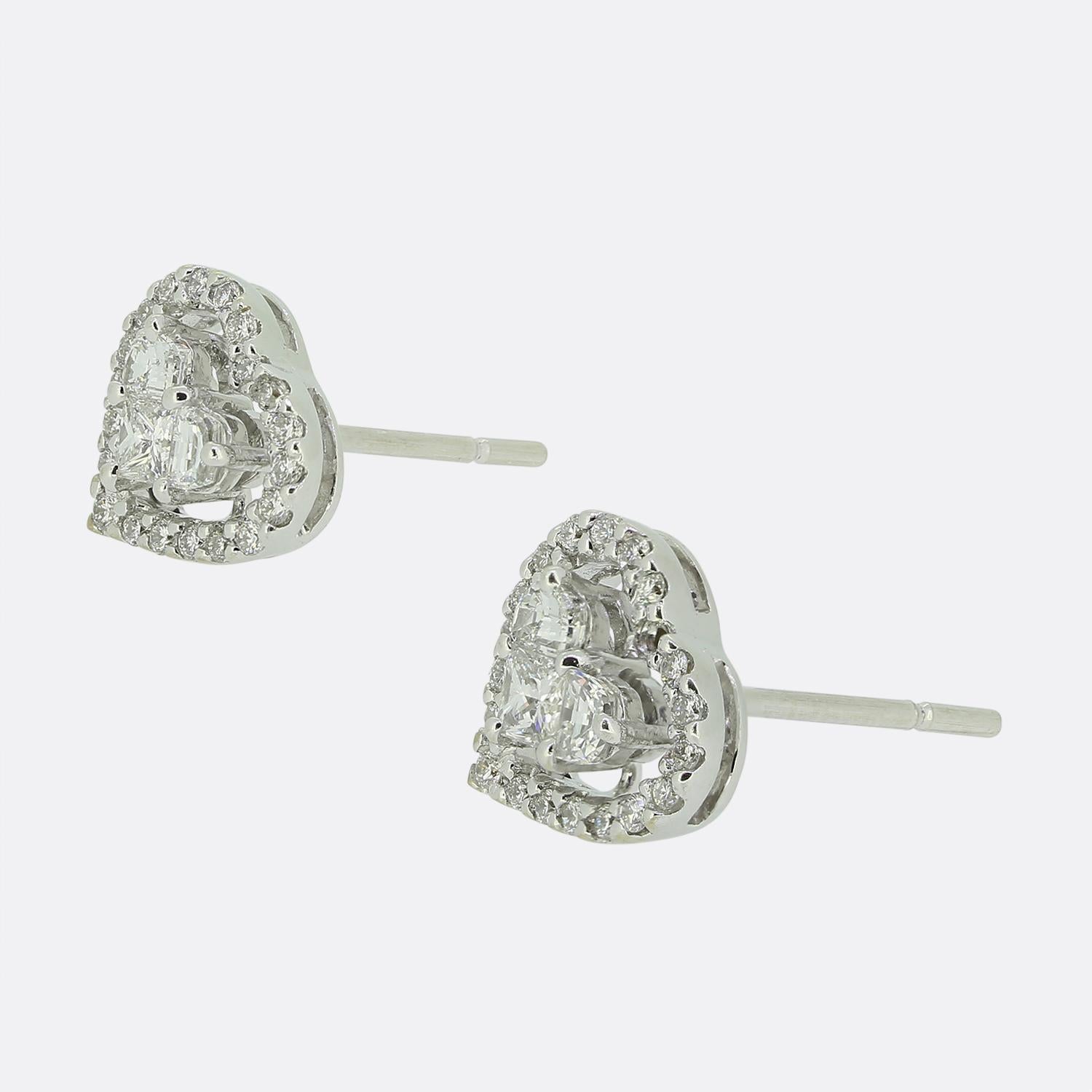Aquí tenemos un encantador par de pendientes de racimo de diamantes en forma de corazón. Cada pieza idéntica de oro blanco de 18 ct está engastada con un único diamante talla princesa de 0,10 ct en el centro. Esta piedra principal está coronada por