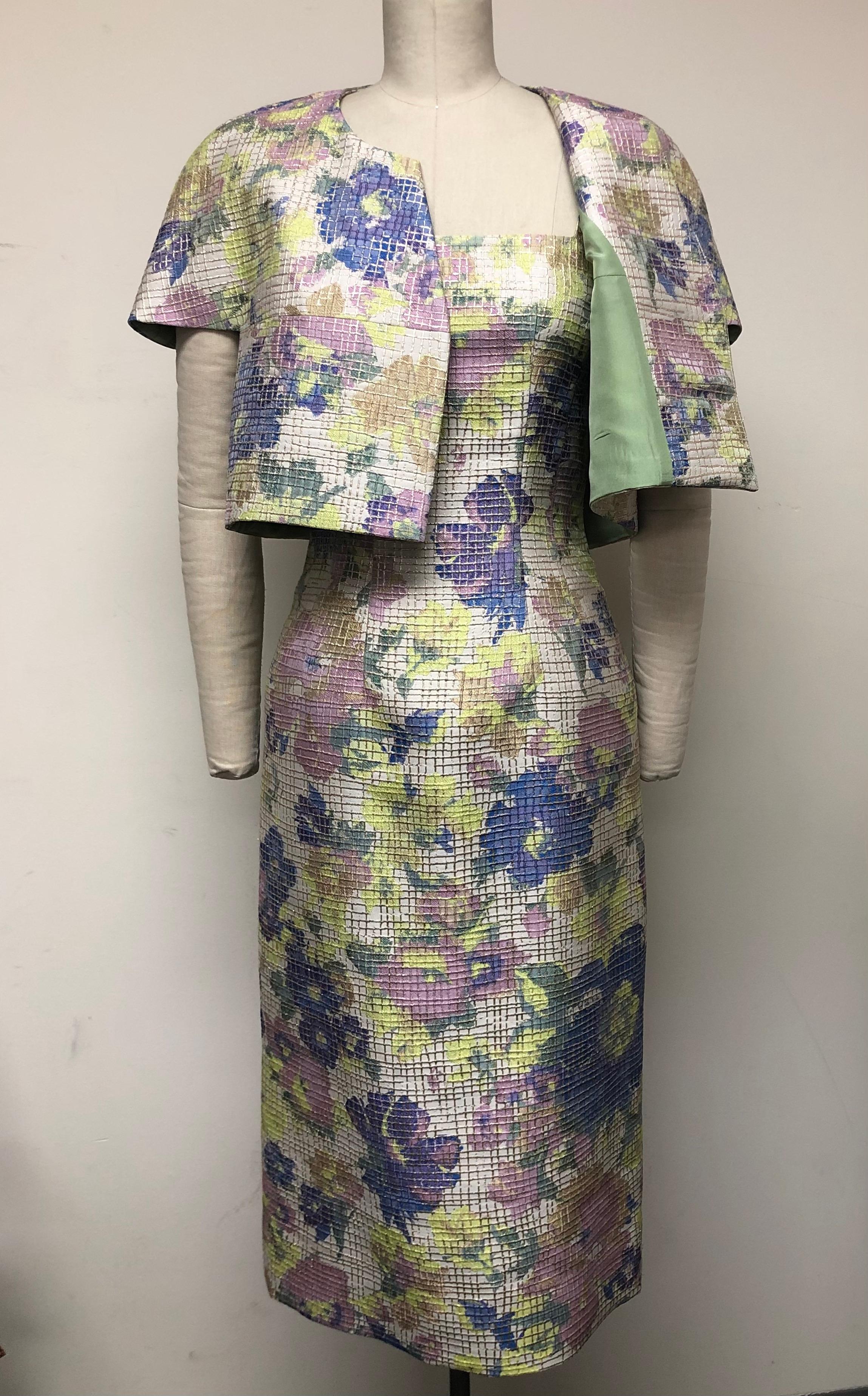 Ensemble dressing at its most elegant! French multi-floral lavender and blue brocade. Wonderfully unique—this fitted square neck slim dress is complemented by a charming matching capelet jacket. The soft floral pattern is enhanced by its metallic