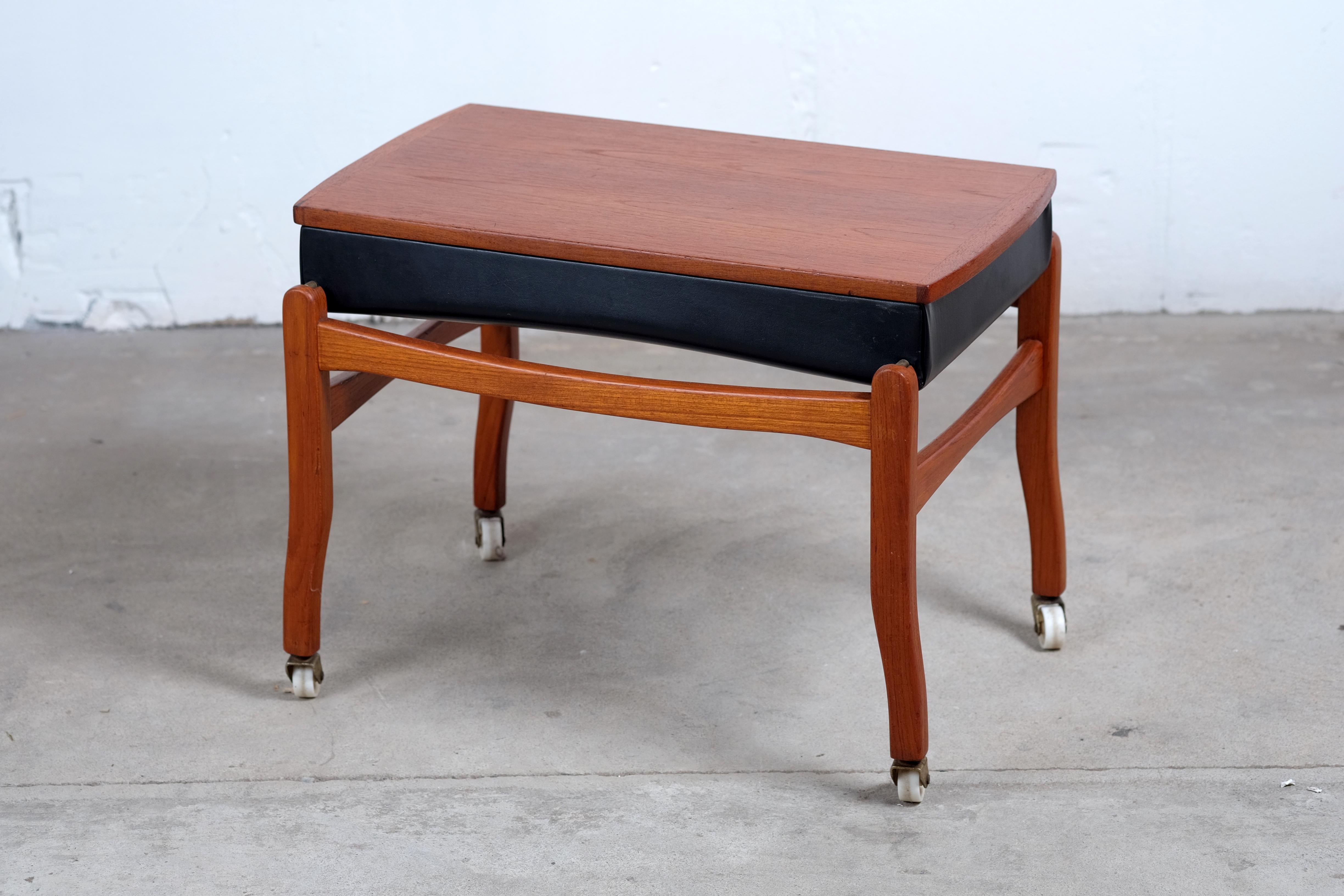 Danish midcentury stool in teak with seat in skai.
The wheels make the stool easy to move around with.
A great detail is that you can turn around the seat and it will act like a coffee table. The stool has some age related wear because of use. But
