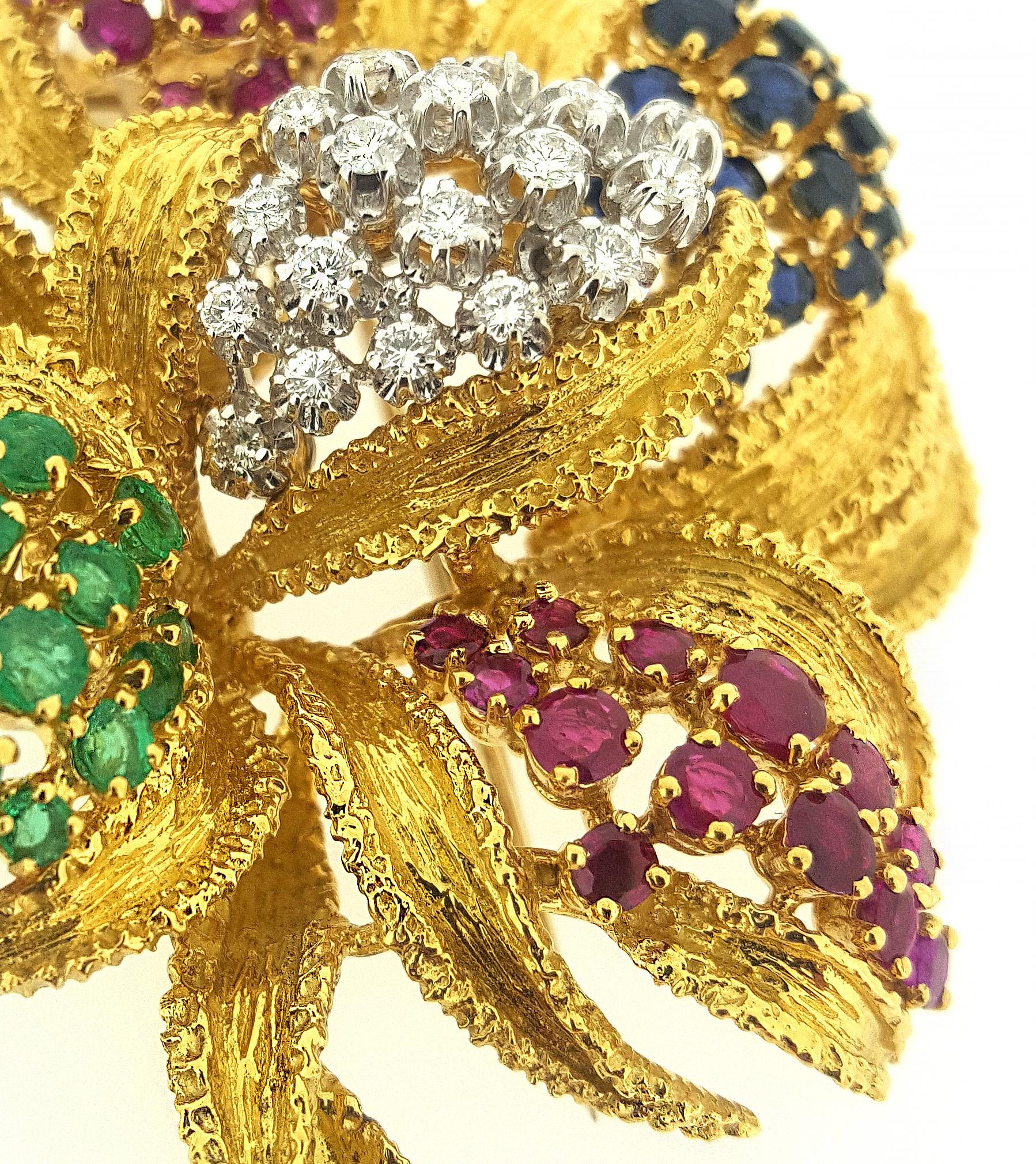 Large multi-gemstone flower brooch featuring emeralds, rubies, and sapphires and .75ctw of sparkling round brillinat cut diamonds set in textured 18kt yellow gold.  Brooch is approximately 2.75 inches long and 2.25 inches wide.  