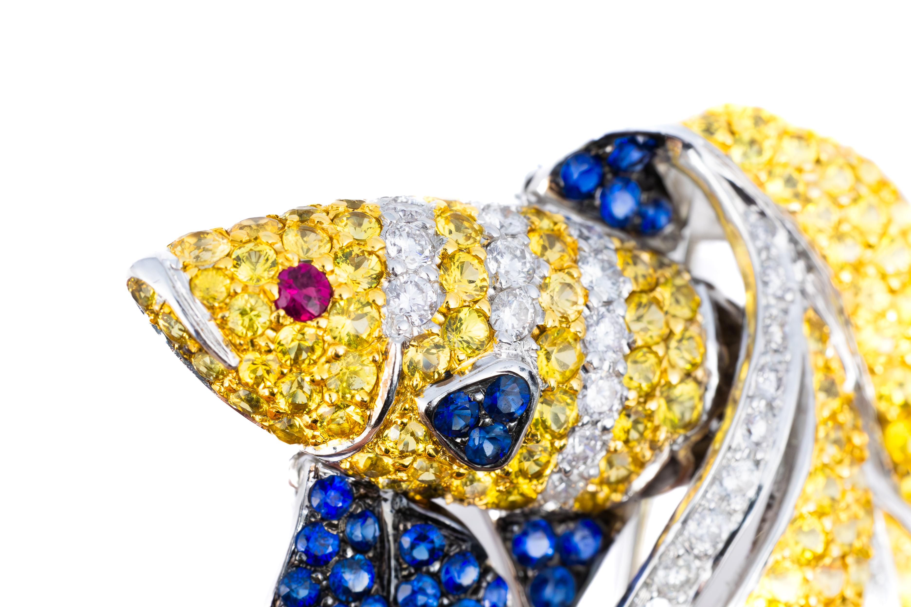 Multi-Gemstone Fish Brooch in White Gold

A dazzling display of artistry and craftsmanship, this captivating fish brooch shimmers with an array of meticulously set gemstones. The body is adorned with a vibrant arrangement of golden-yellow sapphires,