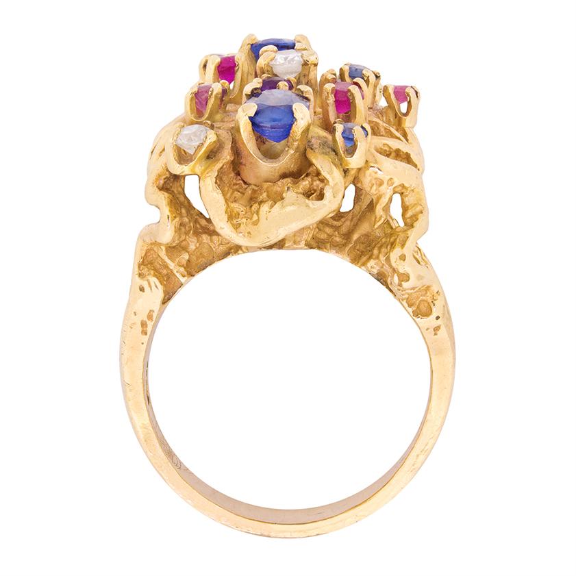 An abstract sculptural form set with a groovy combination of 0.65ct sapphires, 0.24ct diamonds, 0.15ct rubies, 0.05ct emeralds and 0.07ct amethysts in 18 carat yellow gold comprises this bold statement ring, which was crafted during the 1960s in far