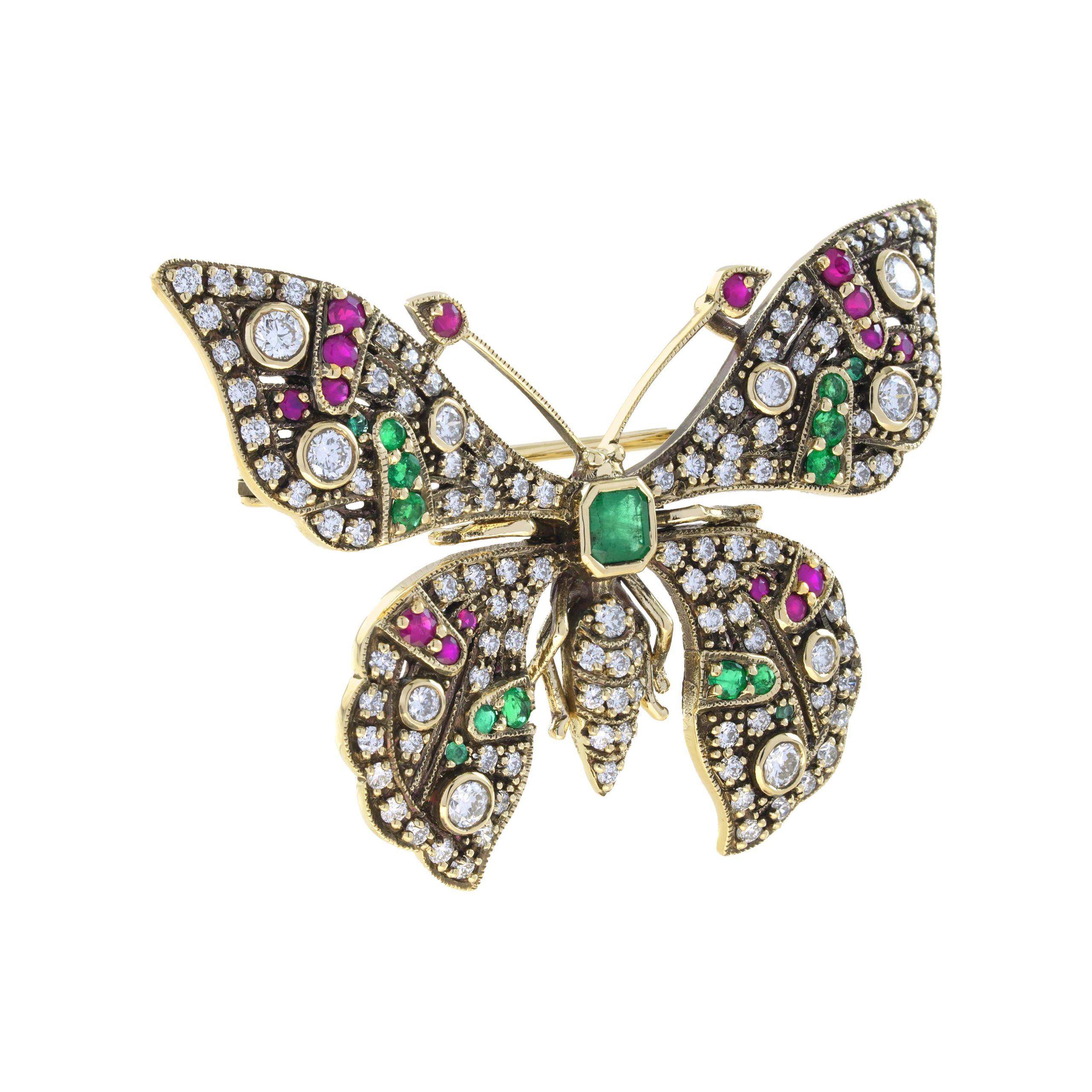 La broche en forme de papillon est finement travaillée en or jaune oxydé 14k. La broche est ornée d'une émeraude verte vibrante de taille asscher pour le corps. Ornée de diamants, de rubis et d'émeraudes sur les ailes, cette broche symbolise la