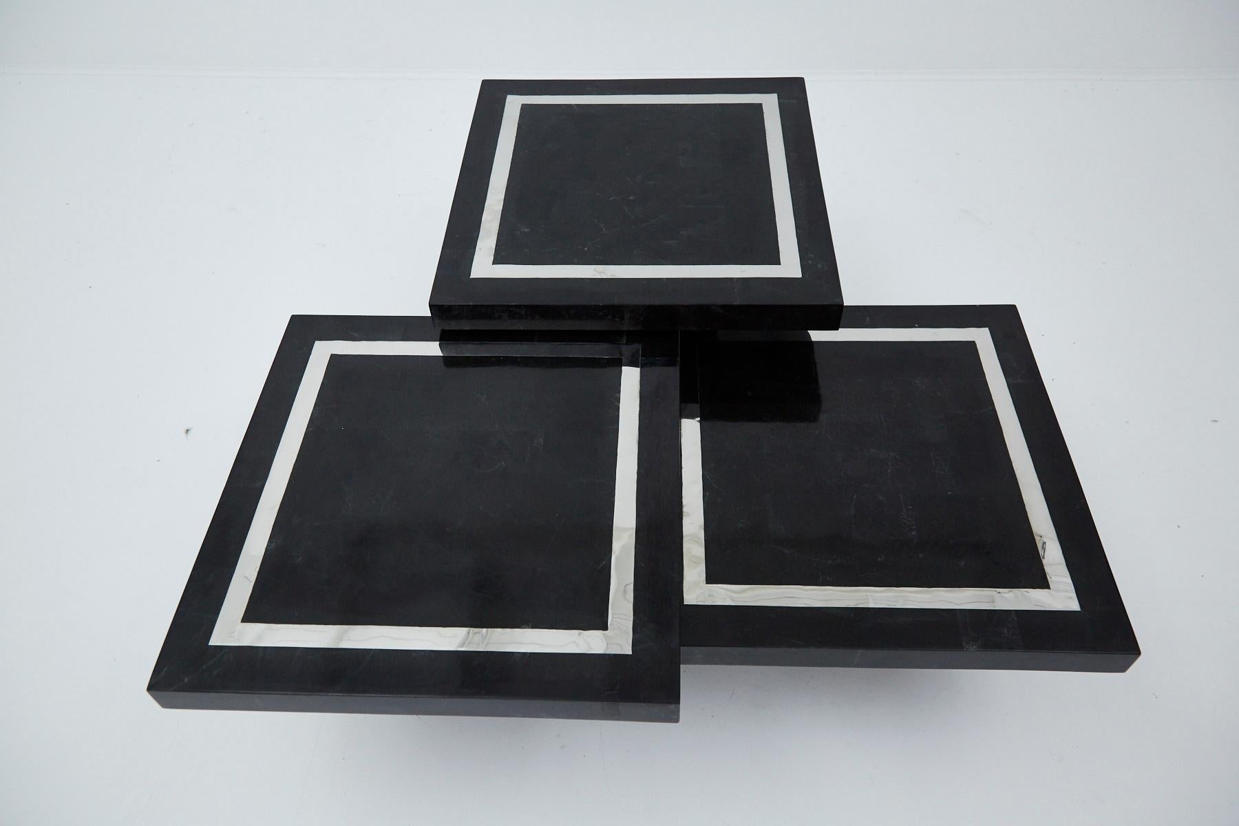 Set of three square mushroom tables of varying heights that can be configured into one larger coffee table. Tables are each comprised of fiberglass with inlaid black tessellated stone throughout, accenting with stainless steel banding to