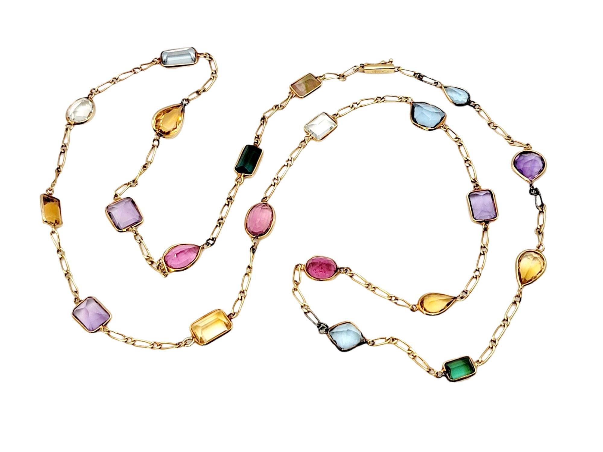 Long, luxurious multi-gemstone station necklace bursting with color. This amazing piece absolutely lights up the neck! Featuring 21 assorted bezel set gemstones on an elongated link chain, the colorful stones pop against the warm yellow gold