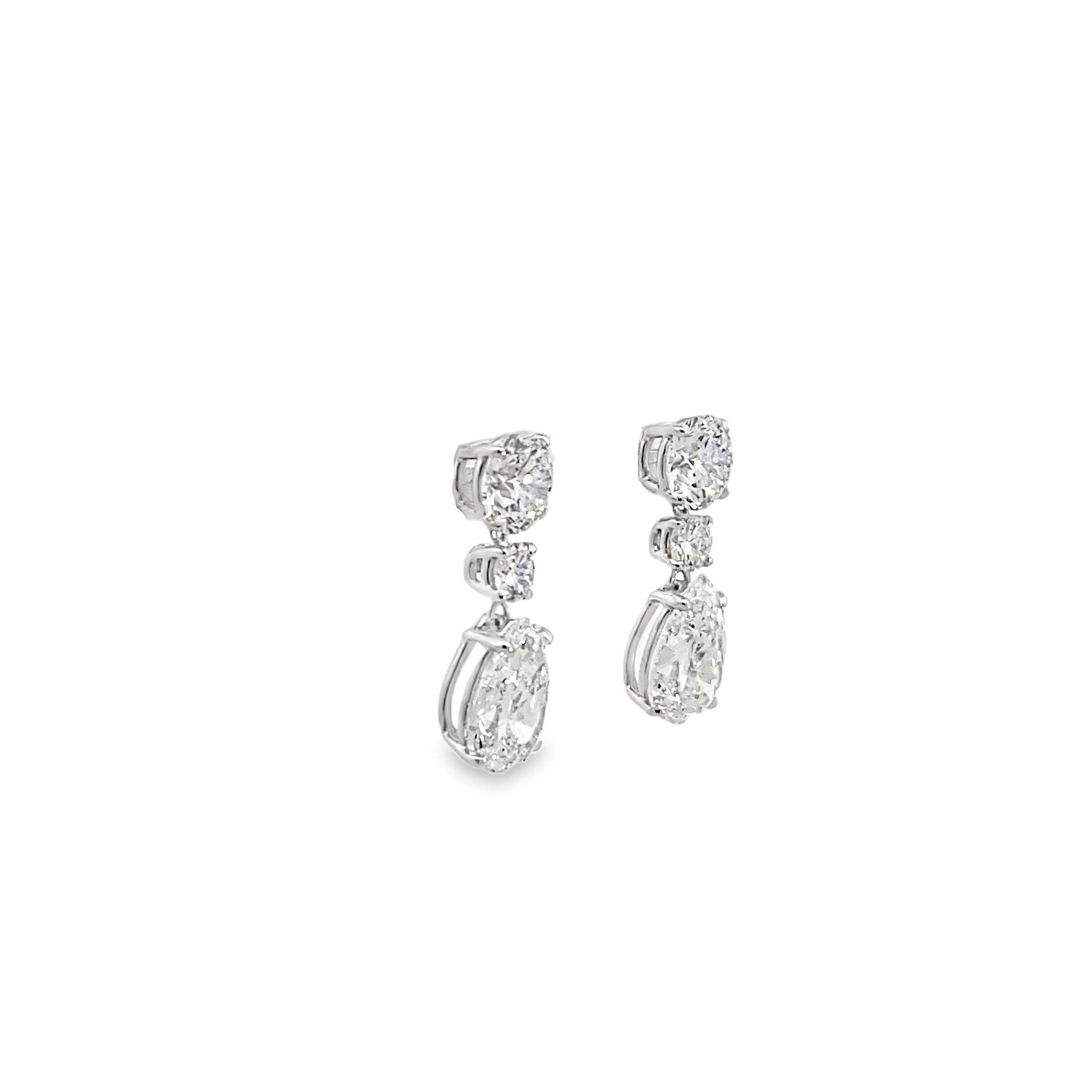 These 18k white gold drop earrings feature a stunning mosaic of prong-set diamonds totaling 6.32 carats. The design incorporates a blend of different diamond shapes, each chosen to maximize brilliance and create a captivating visual effect. The