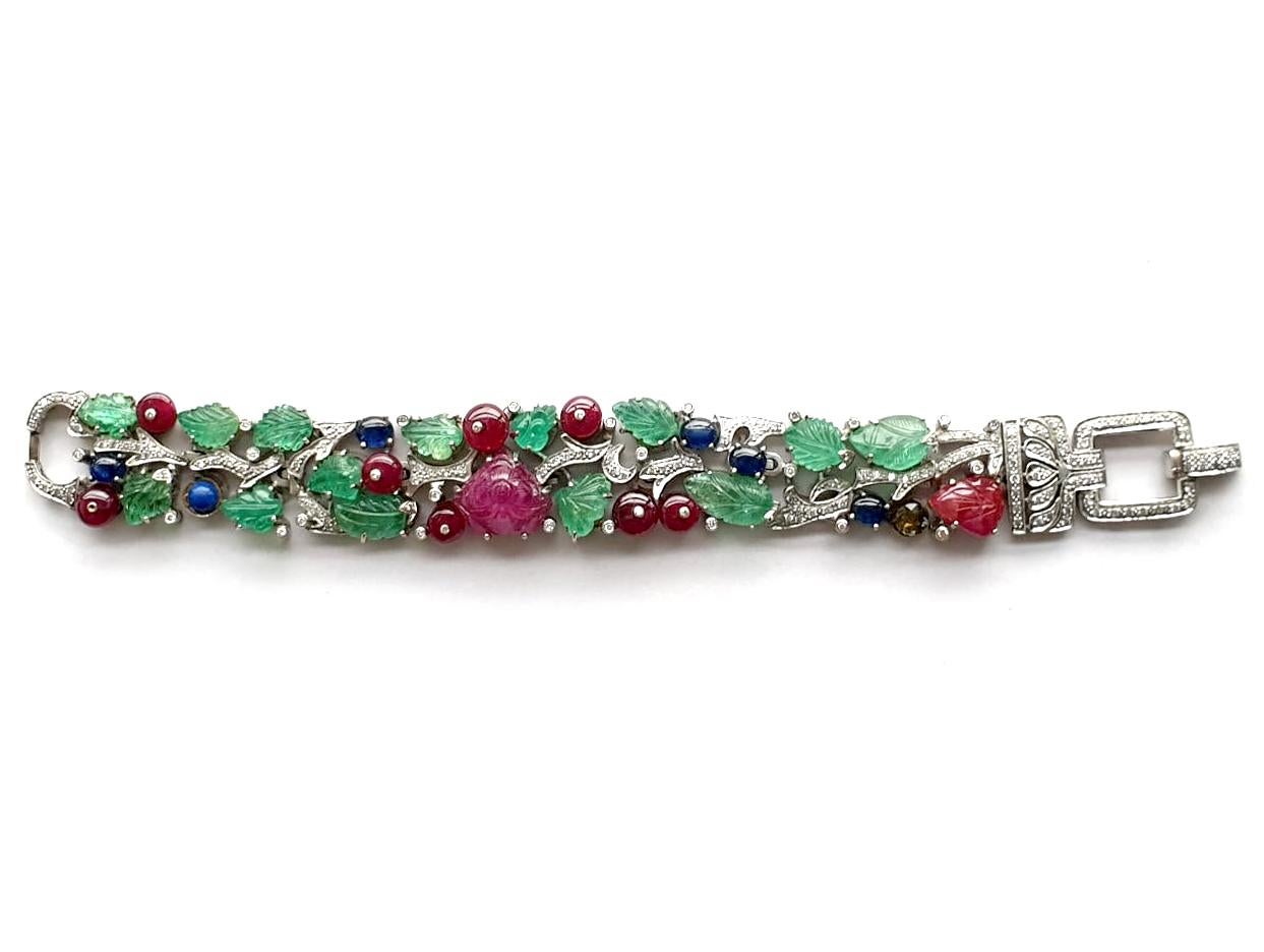 This Emerald, Ruby & Sapphire Bracelet with Diamonds in 18k White Gold is a stunning piece of jewelry that combines the timeless elegance of precious gemstones with the contemporary appeal of white gold. The bracelet features carved leafs in the