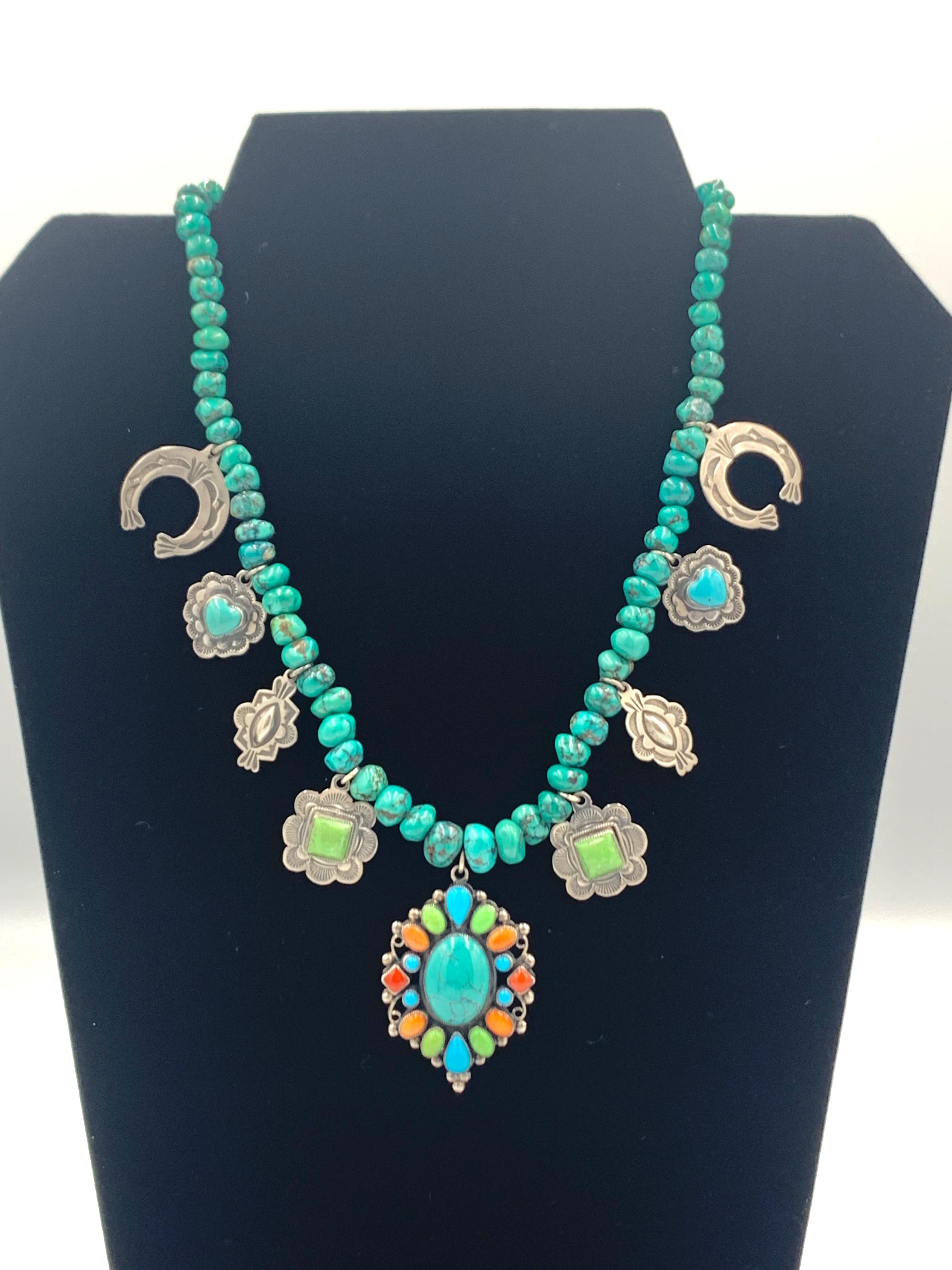 Charm necklace by Arizona silversmith Leo Feeney. The nine charms set in sterling silver are on 16” turquoise beads. The 1 1/4” x 1 5/8” center cluster has a turquoise cabochon, surrounded by turquoise, gaspéite, orange spiny oyster and coral