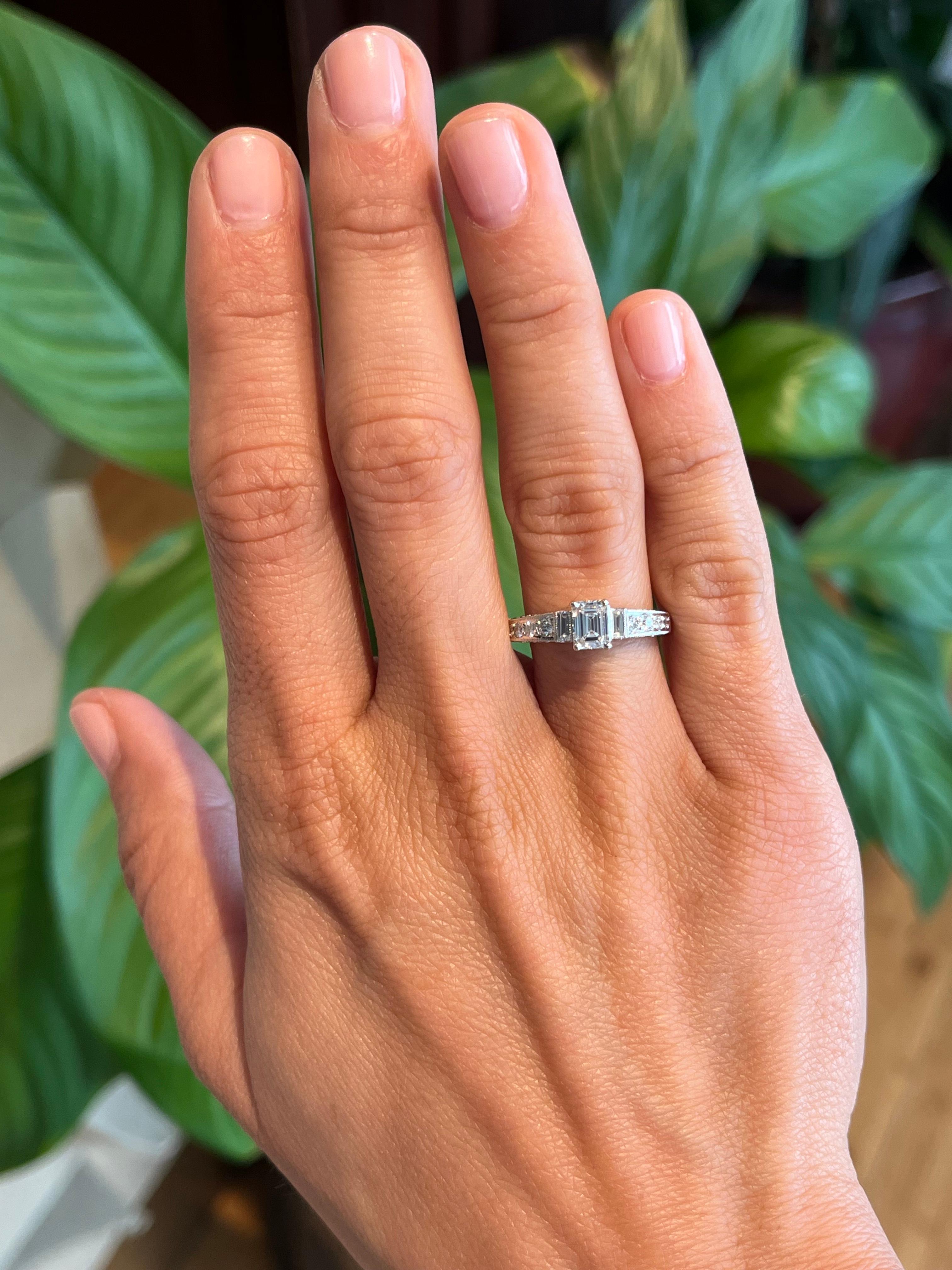 Für alle, die raffinierte Eleganz zu schätzen wissen, bietet dieser Verlobungsring mit mehreren Steinen ein perfektes Gleichgewicht zwischen Art-Déco-Einfluss und zeitgenössischem Design. Der zentrale Diamant im Smaragdschliff (0,48 ct.) wird von