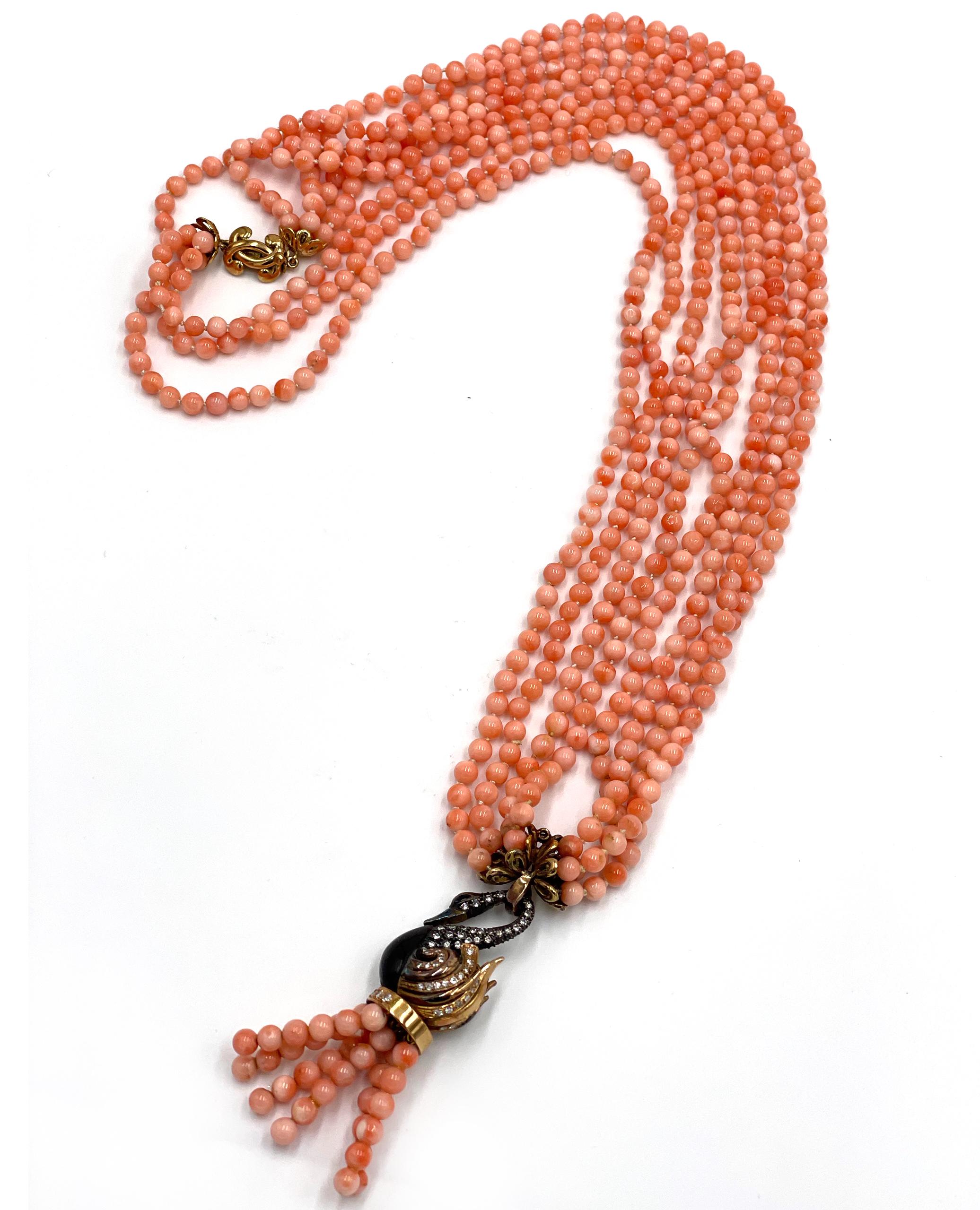 Pre owned vintage esatate 18K yellow gold diamond and angel coral bead tassel necklace.  The necklace has four strands of light orange/pink coral beads ranging from 4.5-4.7mm.
The beads suspend an 18k yellow and black onyx swan that is embellished