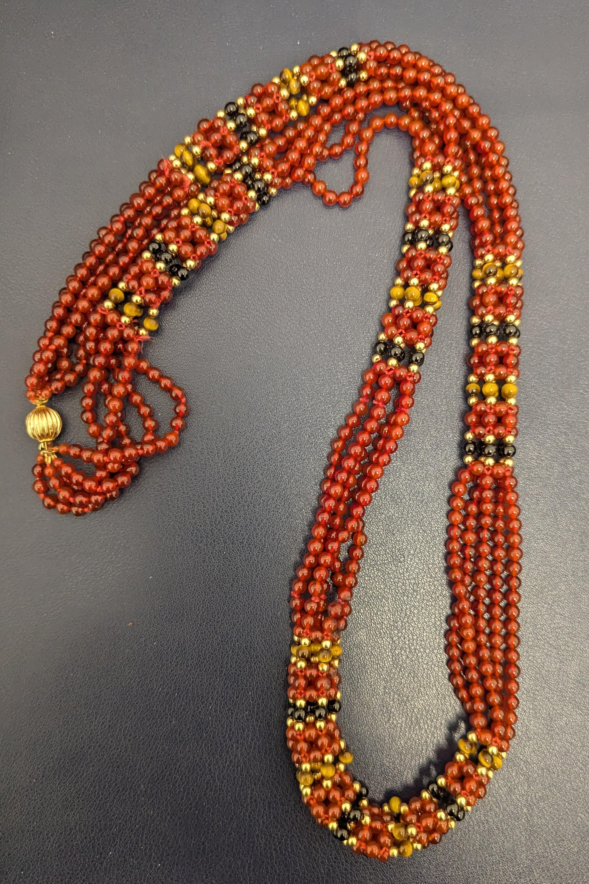 Questa collana presenta cinque lunghi fili di corniola, onice nera, occhio di tigre e perline d'oro, uniti da una chiusura in oro giallo 18 carati. 