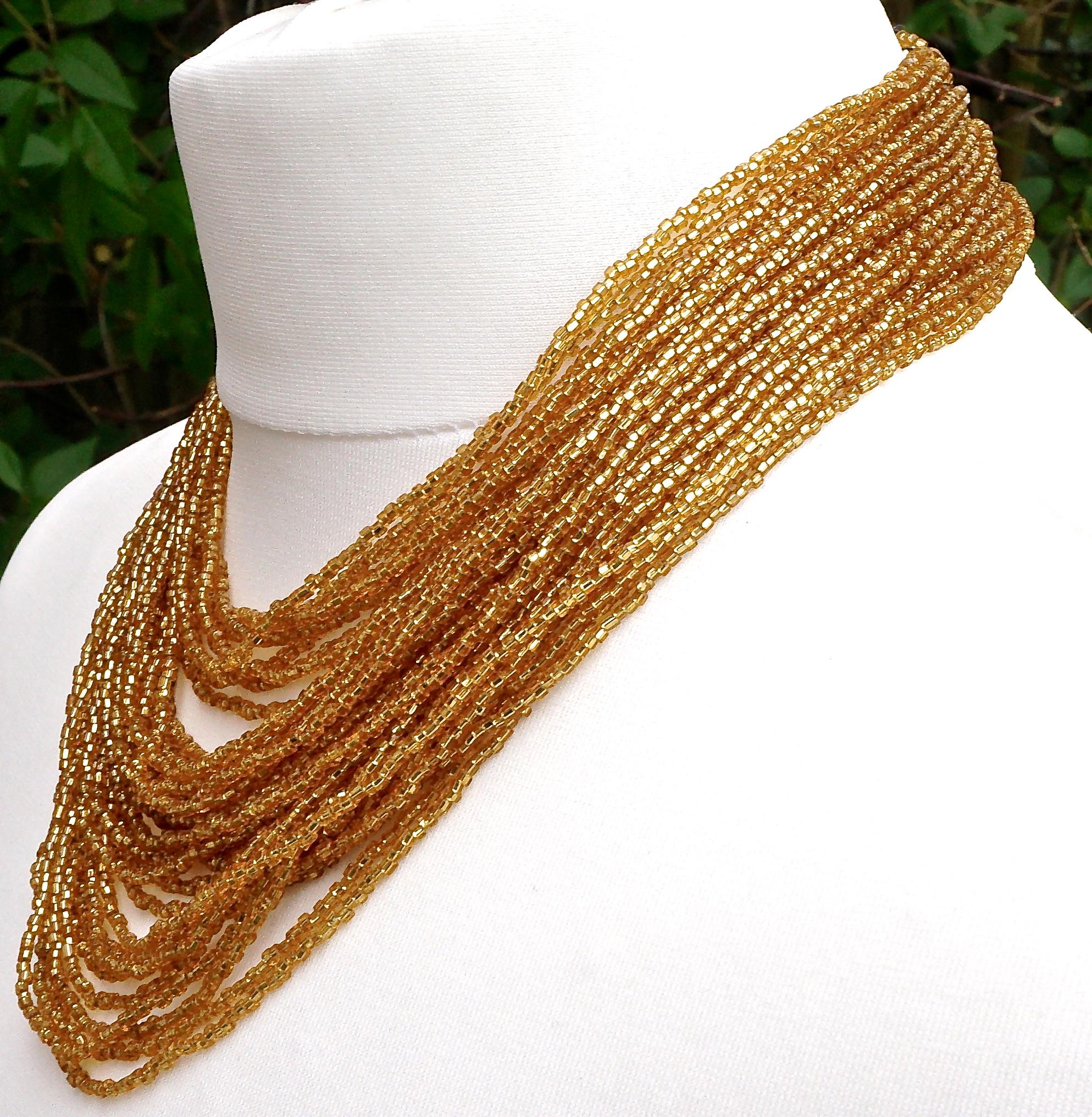 Beautiful multi strand gold glass bead necklace, featuring a large clip clasp with a swirl gold bead design. There are thirty five rows of beads, the shortest length is 41cm / 16.14 inches, and the clasp is 2.9cm / 1.14 inches by 2.2cm / .86cm. The
