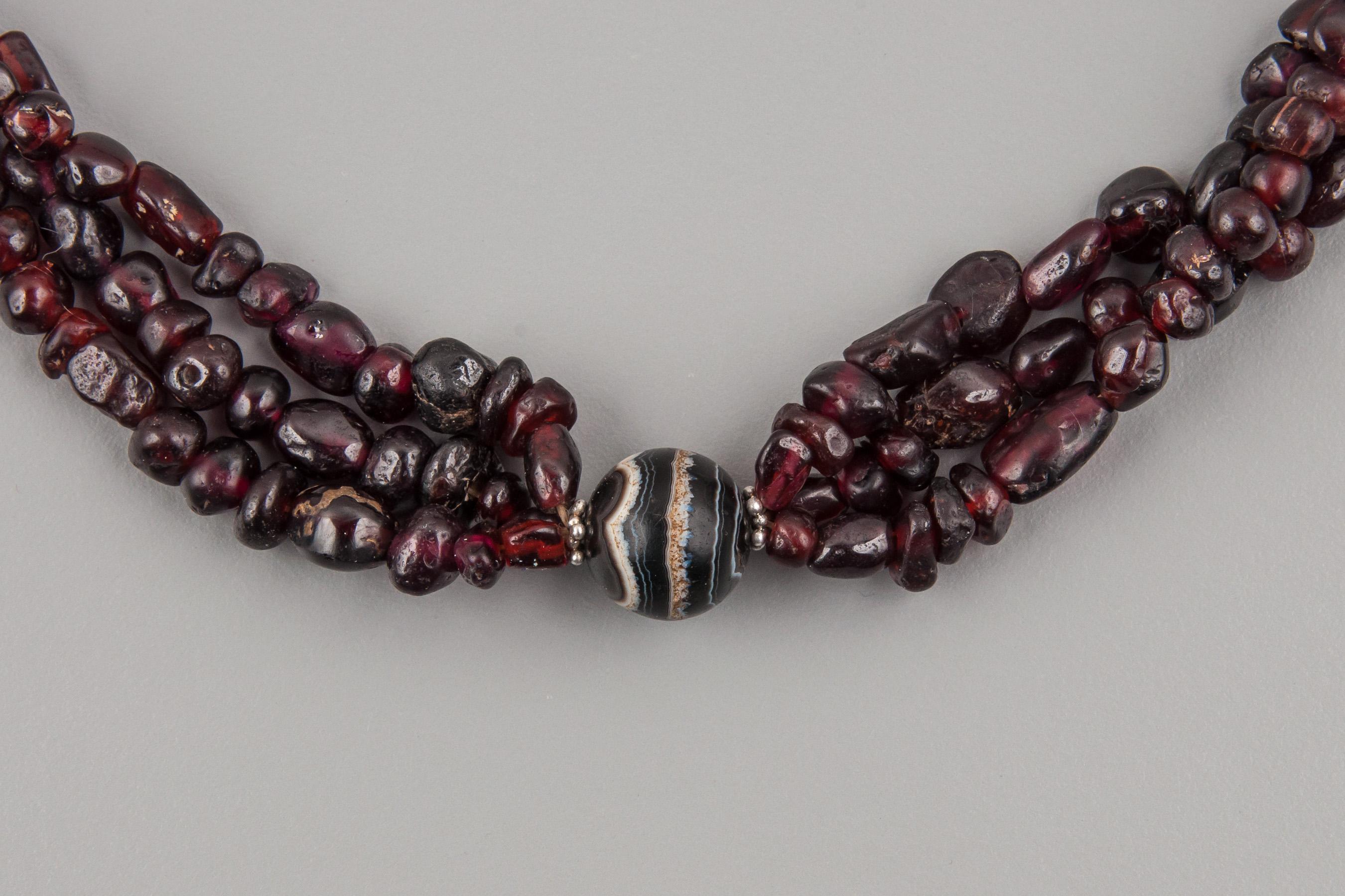 Three strands of ancient garnet beads which are gathered together at five points by five spherical agate beads with white banding. Three of these have lines that encircle the bead and two have banding that goes lengthwise. This produces concentric