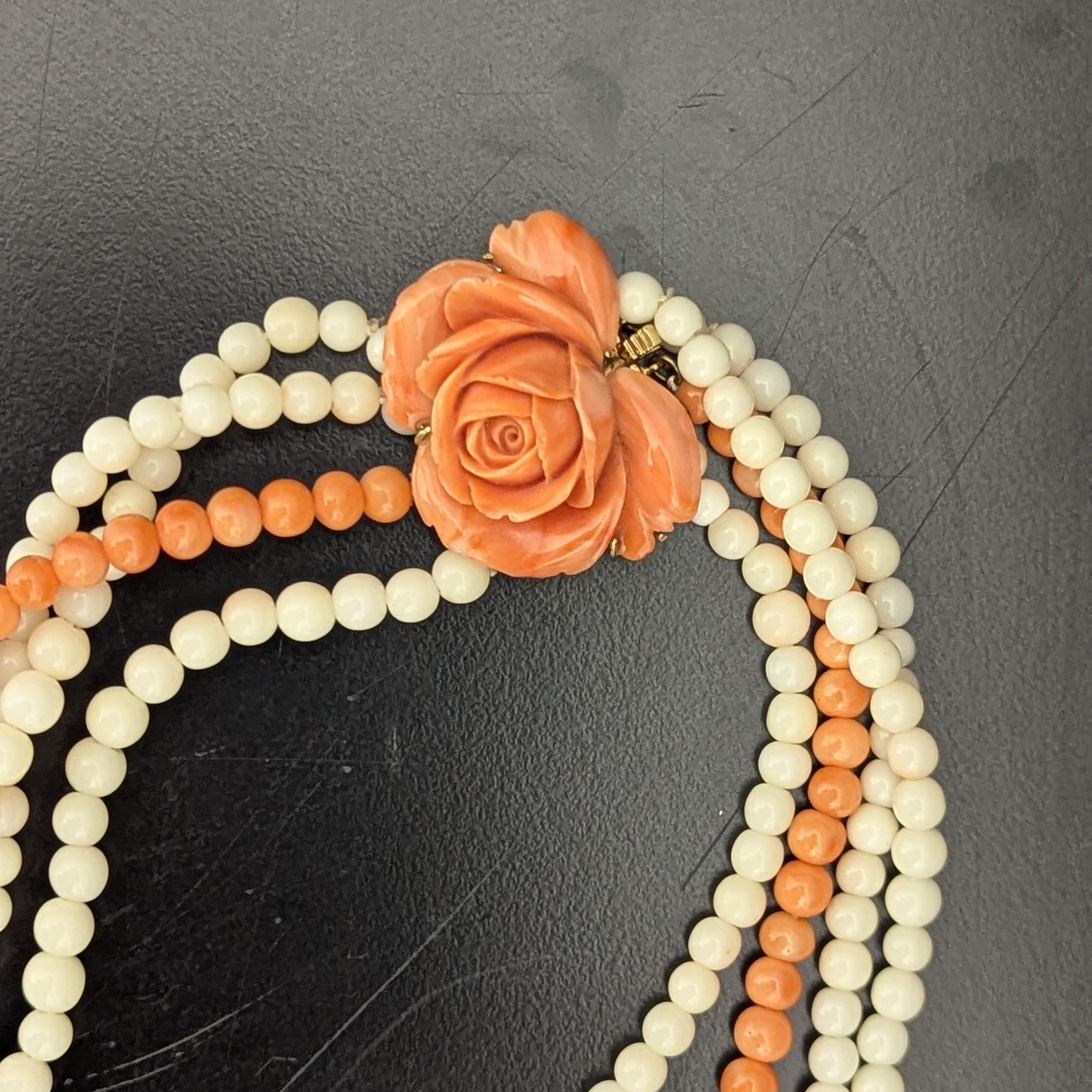 Ce collier à quatre brins présente des perles de corail orange et blanc, mesurant environ 5,0 à 4,0 mm, enfilées ensemble et rencontrées avec un clapet rose en corail sculpté, qui mesure environ 35,0 x 30,0 mm, le tout serti dans de l'or jaune 14K.