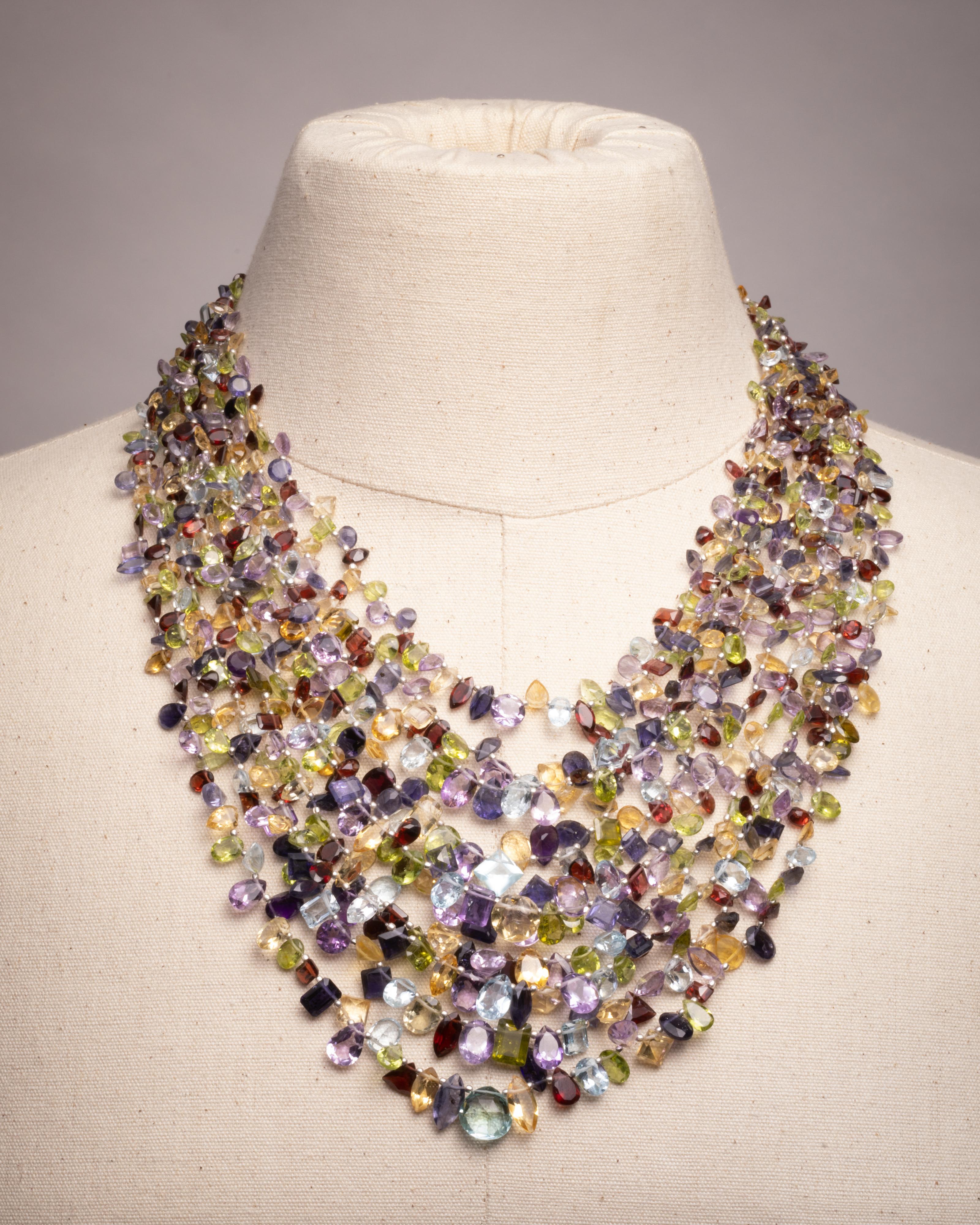 A 10-line multi-strand necklace comprised of faceted semi-precious stones.  Aquamarine, peridot, garnet, citrine, amethyst and kyantie.  Each stone is a different shape--square cut, round, marquise, oval and pear shapes.  Interesting loop clasp also