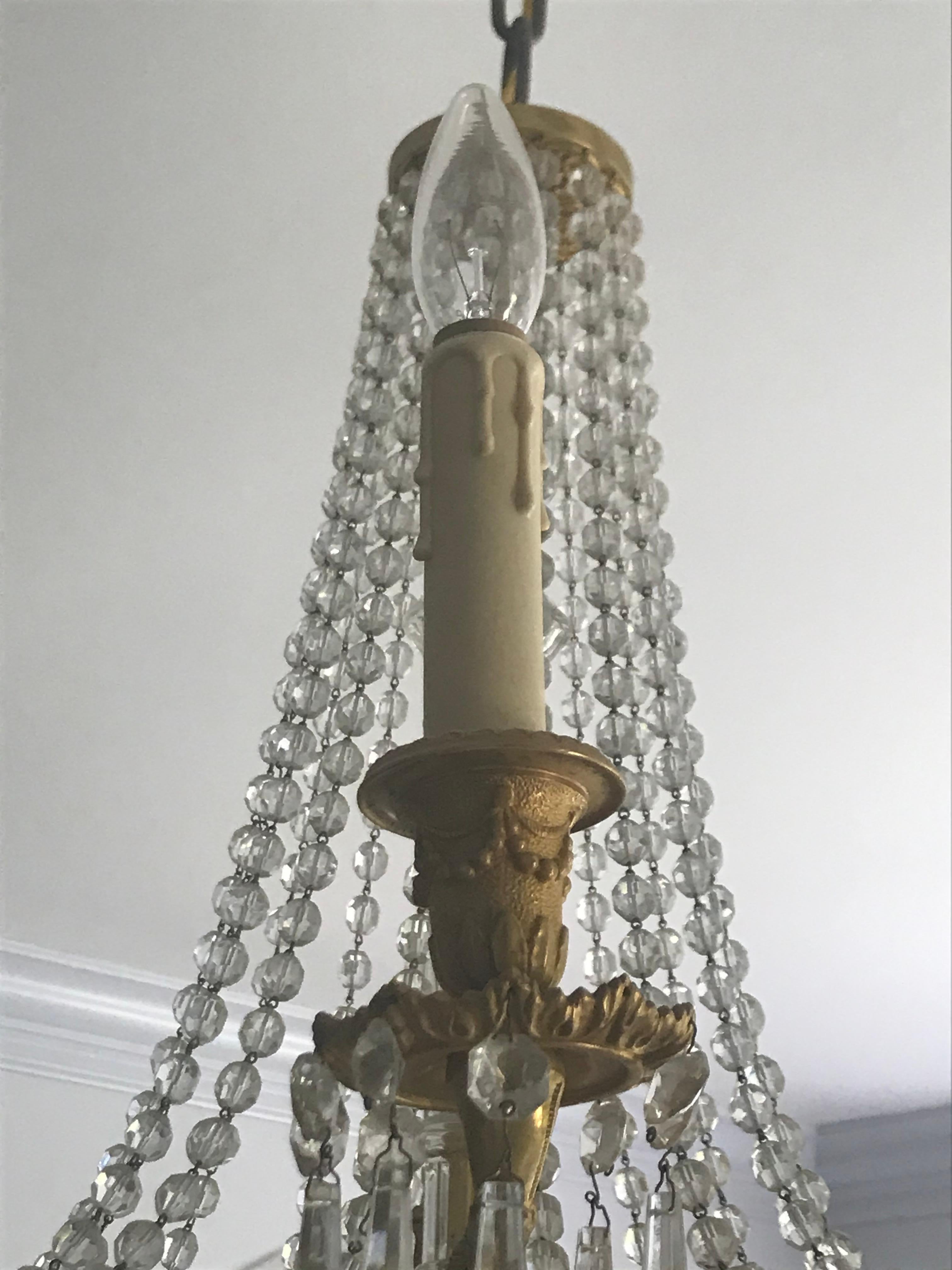 Stunning French gilt bronze multi-tiered chandelier. Circa 1920's, this chandelier features 6 candelabra arms in addition to 4 graduating tiers of crystals. The bronze work is beautifully chased in a drape fashion. The original canopy is beautifully