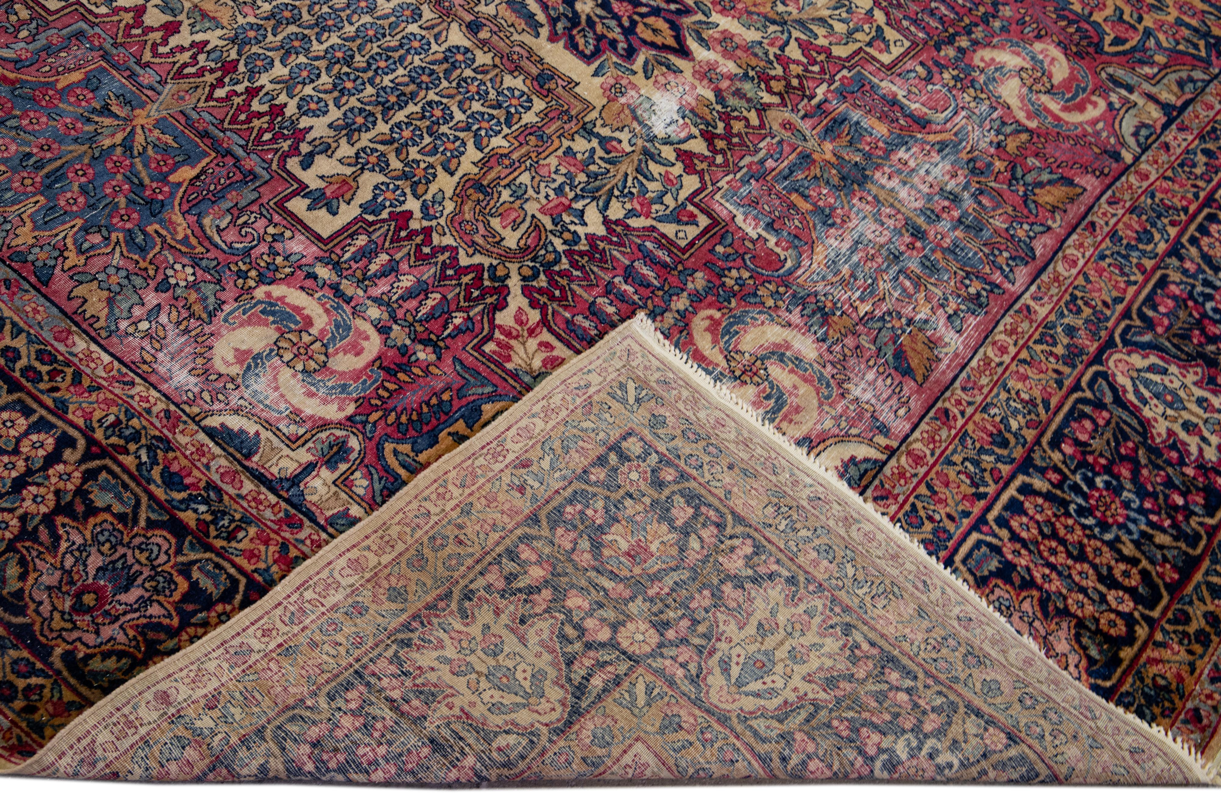 Magnifique tapis antique Kerman en laine nouée à la main avec un champ rose et beige. Ce tapis persan présente un cadre bleu et des accents multicolores dans un magnifique motif floral géométrique à médaillons.

Ce tapis mesure : 8'9