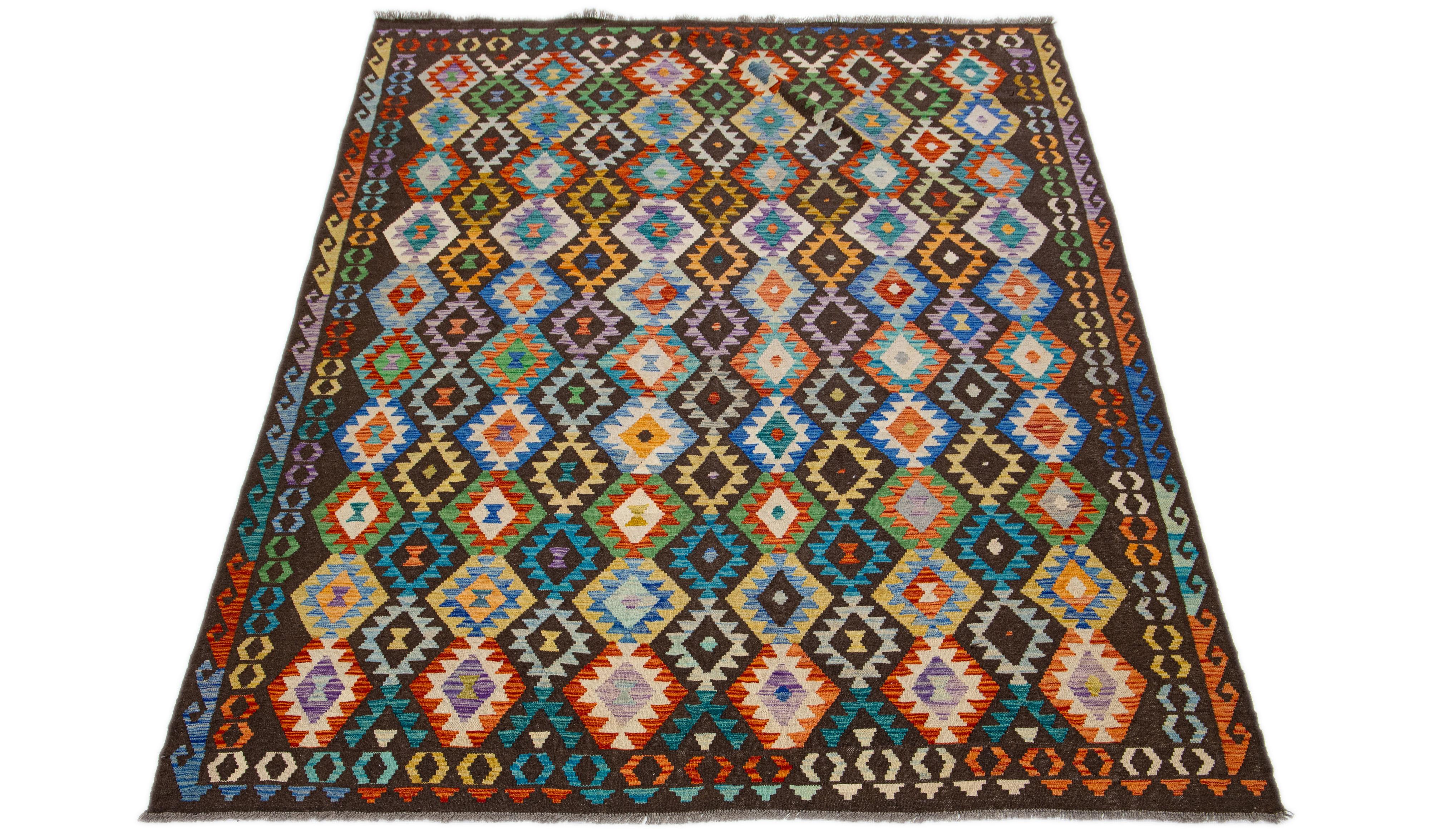 Dieser Wollteppich ist ein brillantes Beispiel für den modernen Kilim-Stil. Es zeichnet sich durch ein lebendiges, mehrfarbiges Feld aus, das bewusst mit einem raffinierten, geometrischen Allover-Muster angereichert ist. Jedes Detail ist sorgfältig