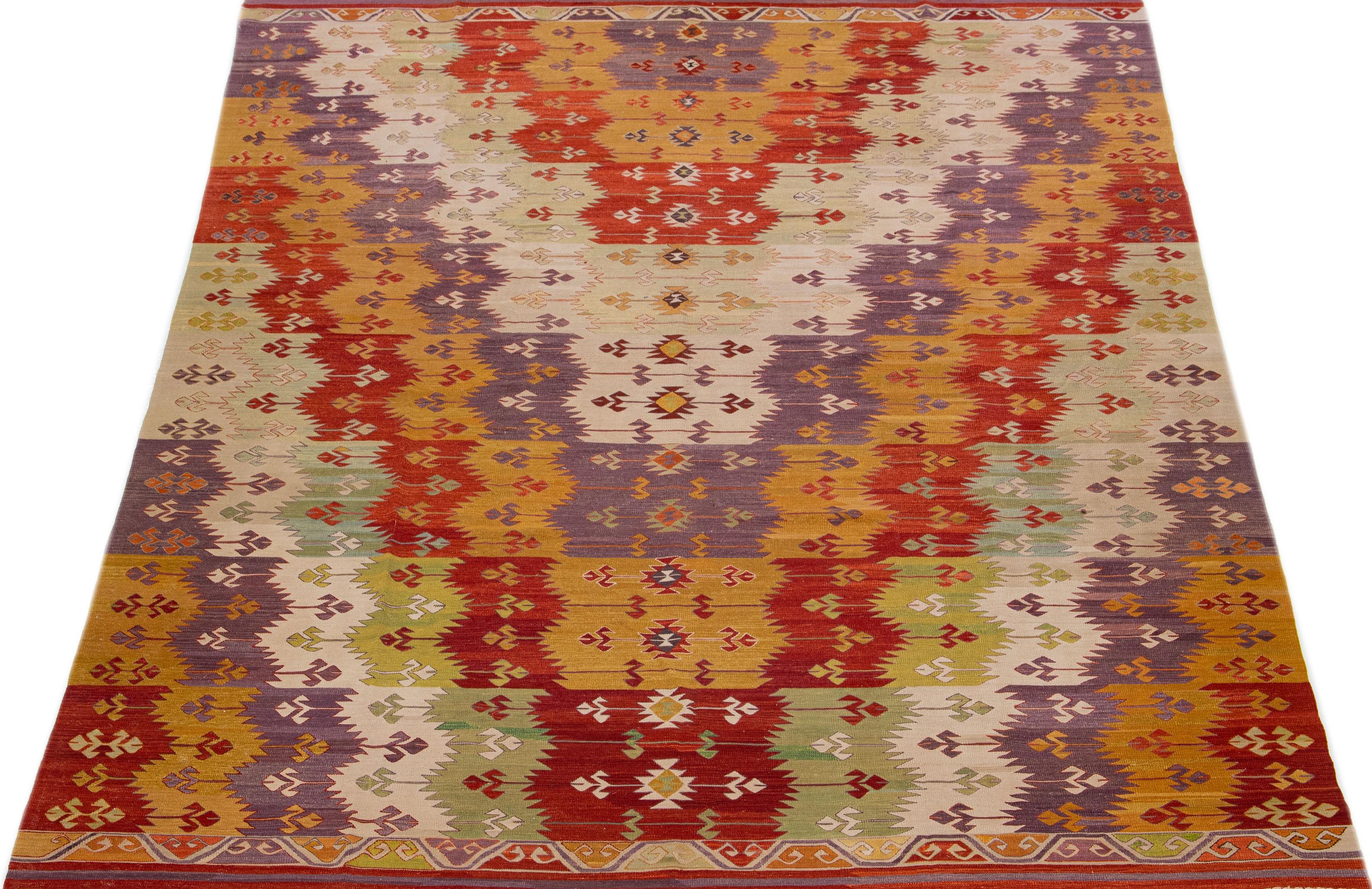 Dieser moderne Kelimteppich türkischer Herkunft zeichnet sich durch ein lebhaftes und komplexes geometrisches Muster aus, das die Farben Rot, Grün, Violett und Orange kombiniert und so eine zeitlose Ergänzung für die Inneneinrichtung des 21.