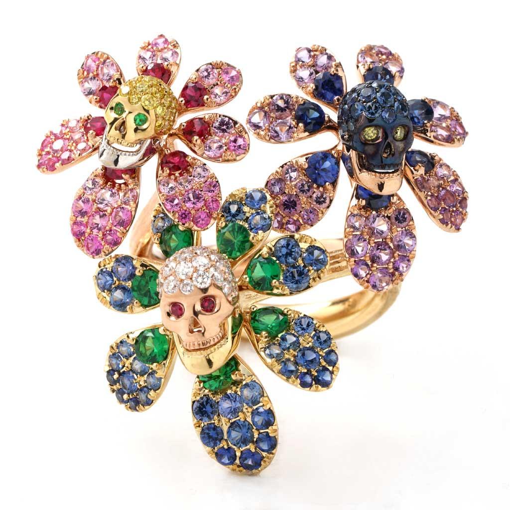 Dieser einzigartige Ring ist aus zweifarbigem 18-karätigem Gold gefertigt und wiegt ca. 15 Gramm. Dieses festliche und farbenfrohe Bouquet aus mehrfarbigen Edelsteinen und Diamanten ziert 3 Totenkopf- und Blumenmotive und erinnert an den Dia De Los