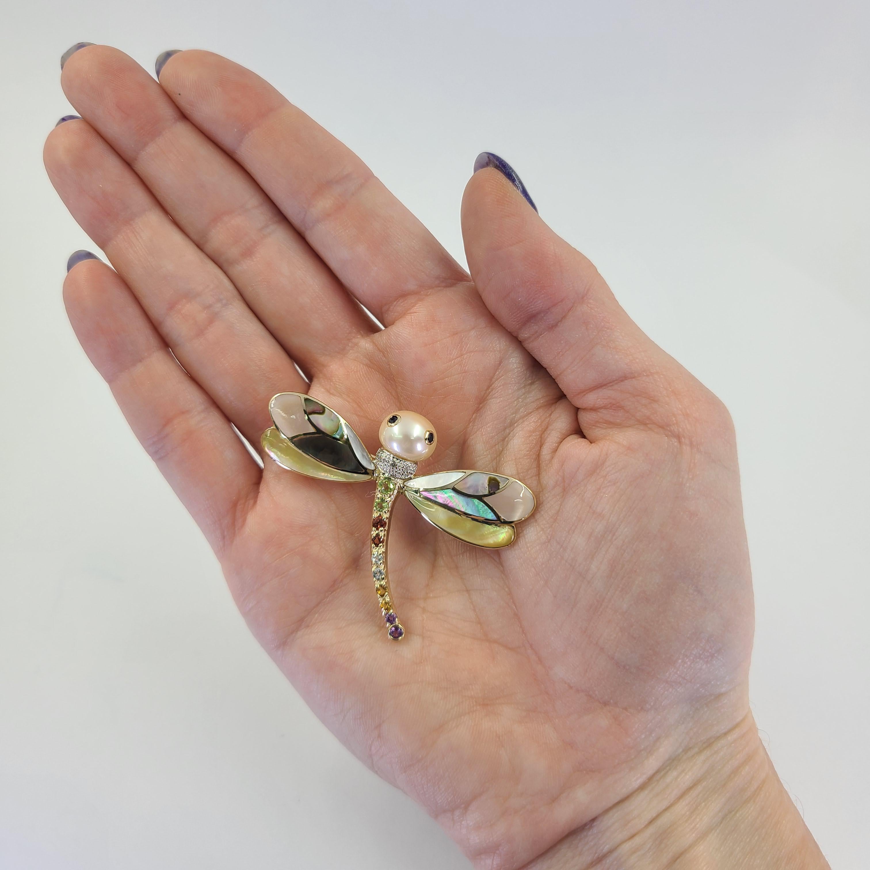 14 Karat Yellow Gold Dragonfly Pin Featuring A Cultured Pearl Head, Mother-of-Pearl Inlay Wings, and Gemstone Set Body (Diamonds, Peridot, Garnet, Blue Topaz, Citrine, and Amethyst). 2 Inches Wide By 1.5 Inches Long. Finished Weight Is 6.0 Grams.