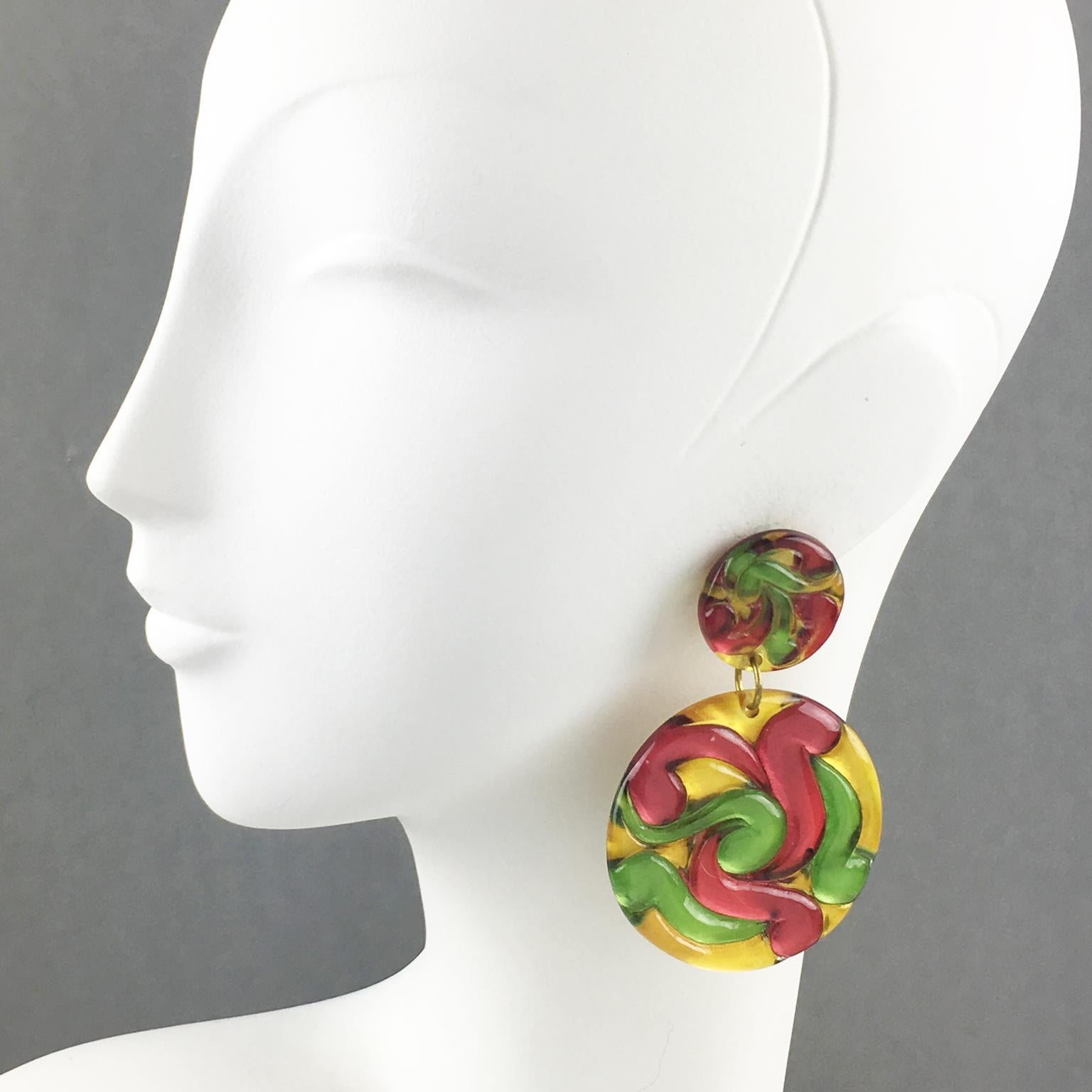 Lovely oversized Lucite clip-on earrings. Huge disk dangling shape featuring dimensional carving with multicolor swirling. Assorted paint colors of yellow mustard, apple green, and raspberry red. There is no visible maker's mark.
Measurements: 3.19