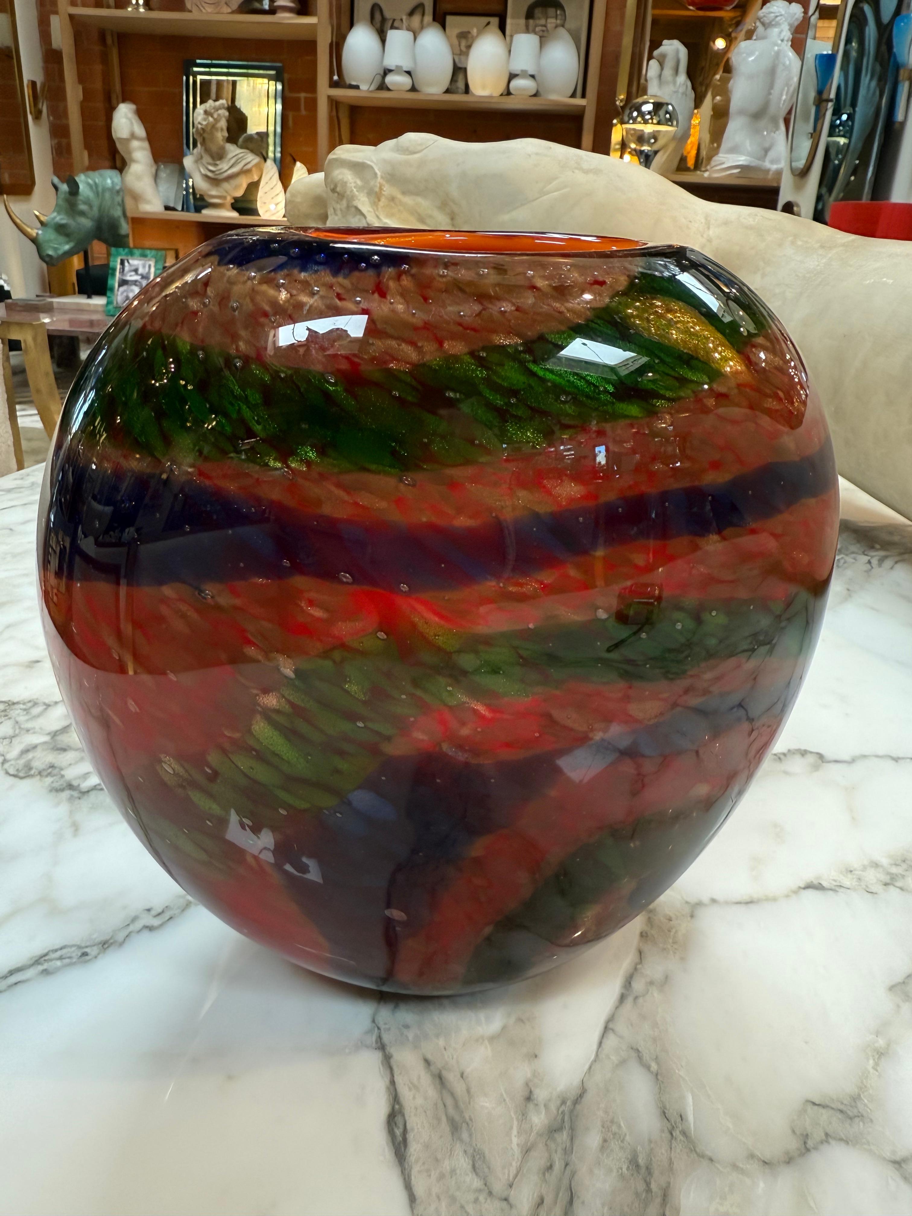 Questo splendido vaso in vetro artistico di Murano mette in mostra l'eccezionale maestria dell'arte vetraria veneziana. Soffiato a mano da abili artigiani, il vaso presenta una vibrante tavolozza multicolore con toni dominanti di rosso fuoco,