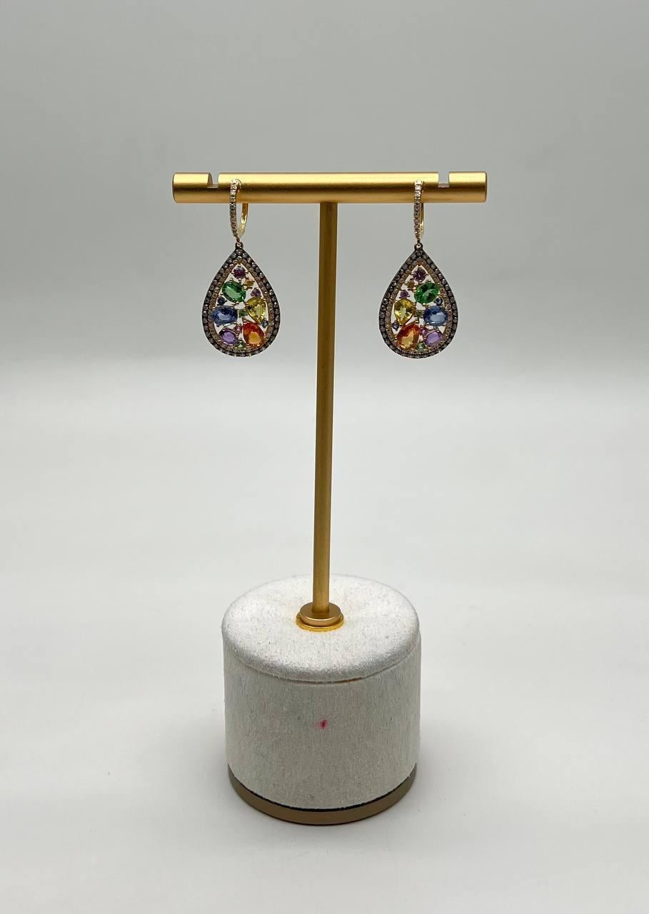 These earrings showcase a teardrop design adorned with multicolored sapphires. The vibrant stones are set within a delicate border of smaller, sparkling diamonds. The earrings hang elegantly from a simple hinged huggie, adding a touch of