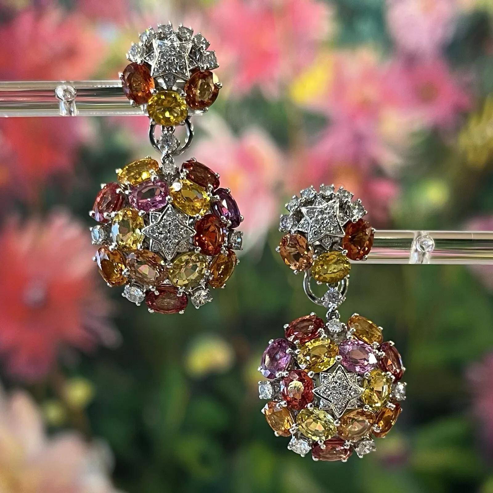 Multicolor Sapphire and Diamond Star Drop Earrings in 18k White Gold 

Natural Sapphire and Diamond Earrings features 32 multi-color natural Sapphires, oval-shaped, with tones of orange, yellow, and pink accented by Round Brilliant Diamonds set in