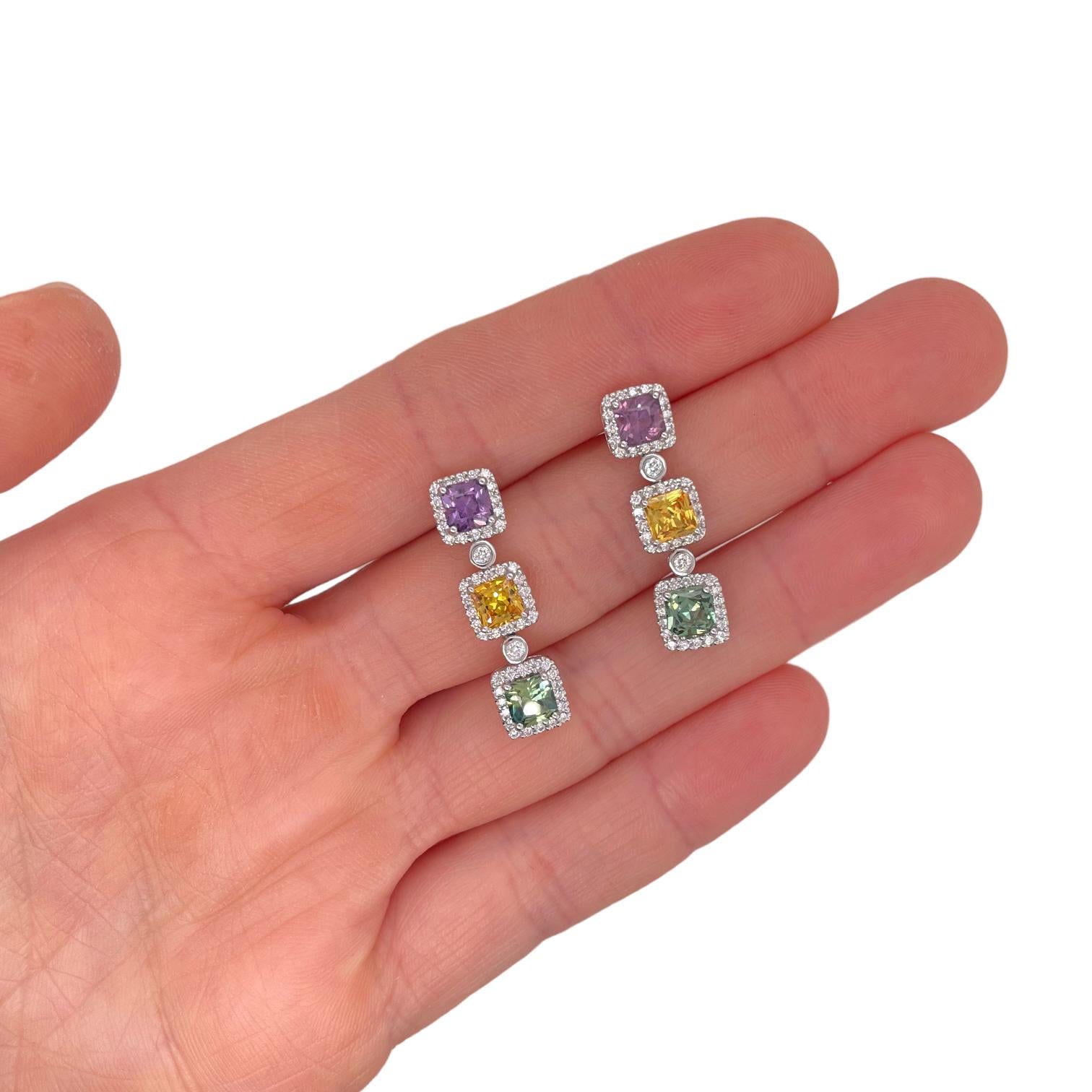 One of a kind earrings contain six square radiant cut multi color sapphires (purple, green and yellow) weighing a total of 4.20cts.
Stones are surrounded by round brilliant diamonds creating a halo design, 0.75cts total diamonds within earring. All