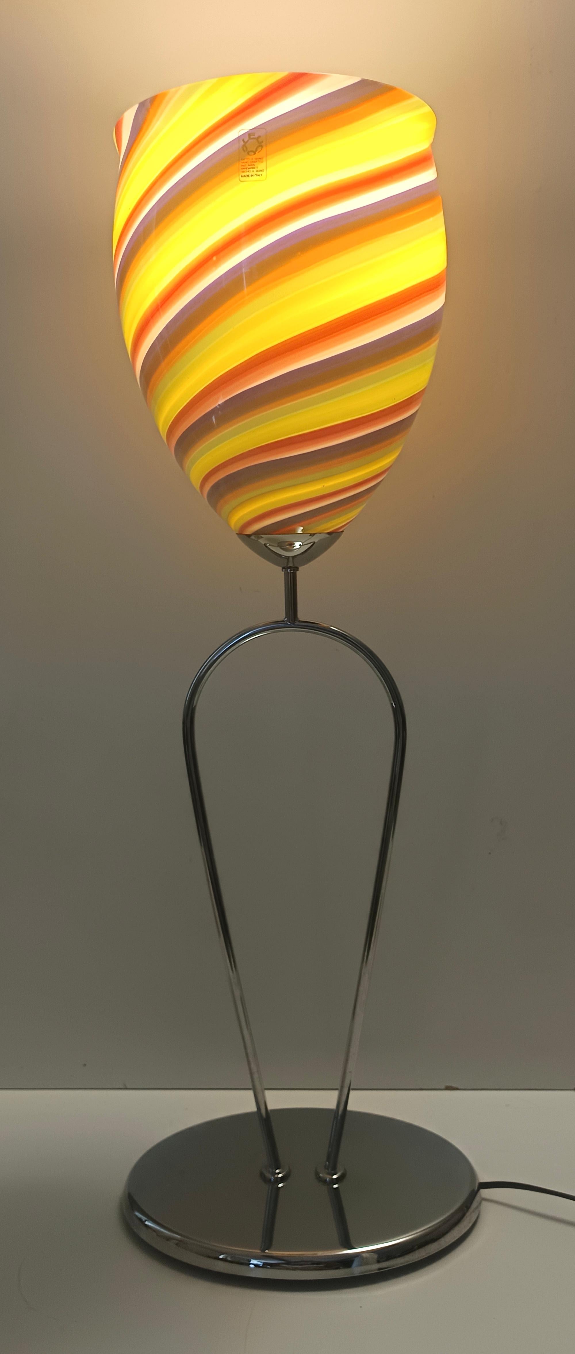 1980s, made in Italy. 
This table lamp features a metal stem and a multicolored Murano glass lampshade with turned canes.
The base is oval.
It is labeled Leucos, which is a prestigious Italian company that often collaborated with Vetreria Toso. The