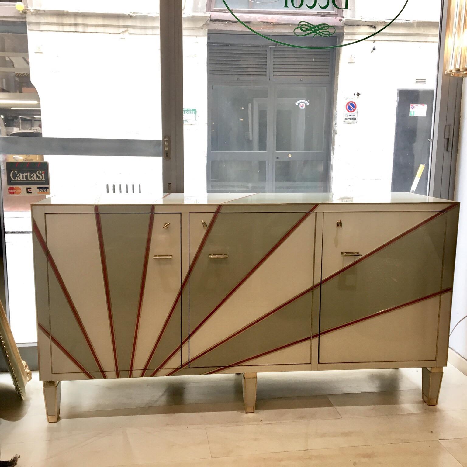 Multicolored opaline glass credenza with geometrical design and brass edges. The wooden structure is covered with ivory, grey and red opaline glass. The red opaline glass is the edge that delimits the geometrical design. The credenza has three doors