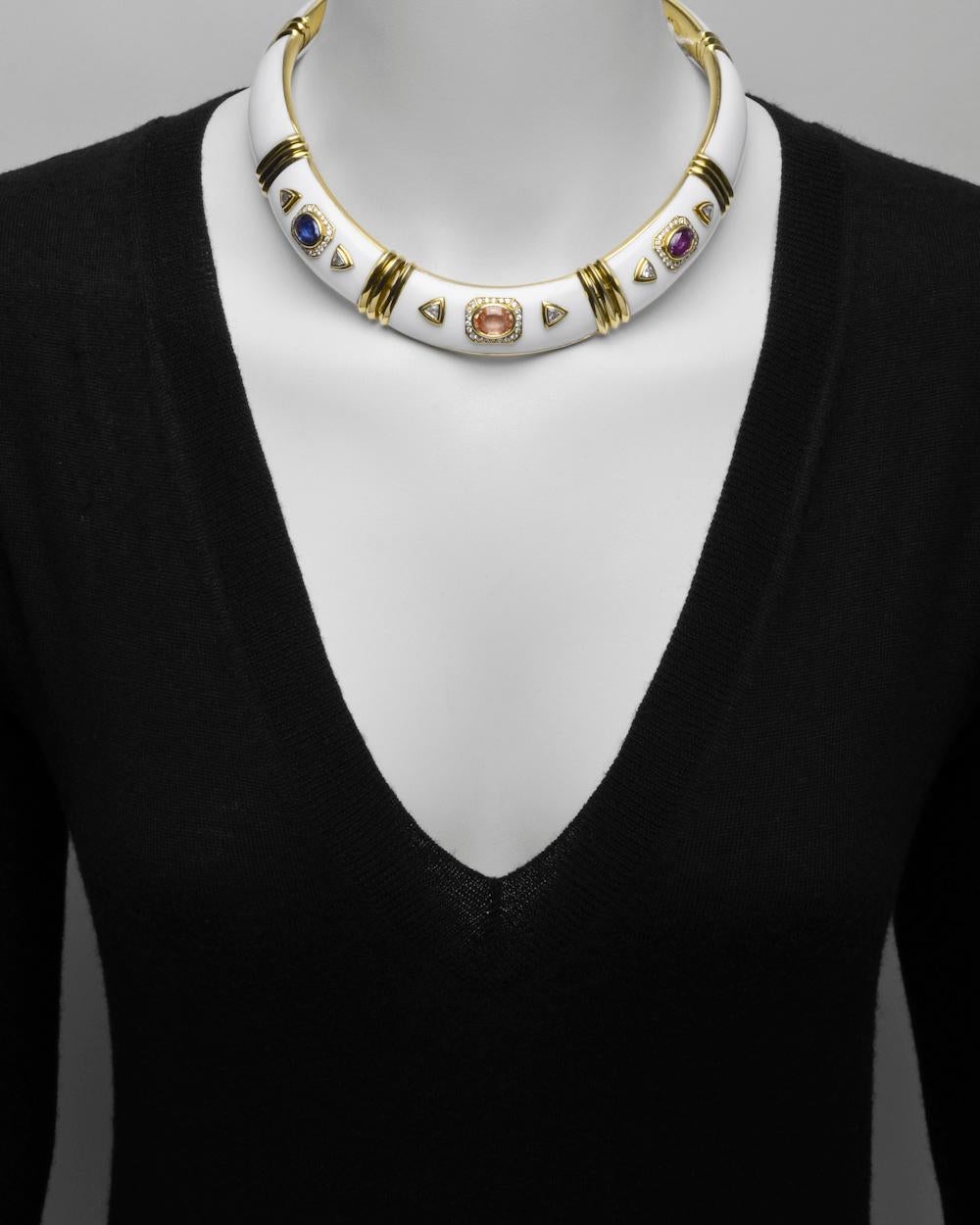 Collar necklace with matching ear clips, in 18k yellow gold and white enamel. The necklace set with an oval-shaped blue, peach-toned and pink sapphire together weighing approximately 10.00 total carats accented by trillion-cut and round-cut diamonds