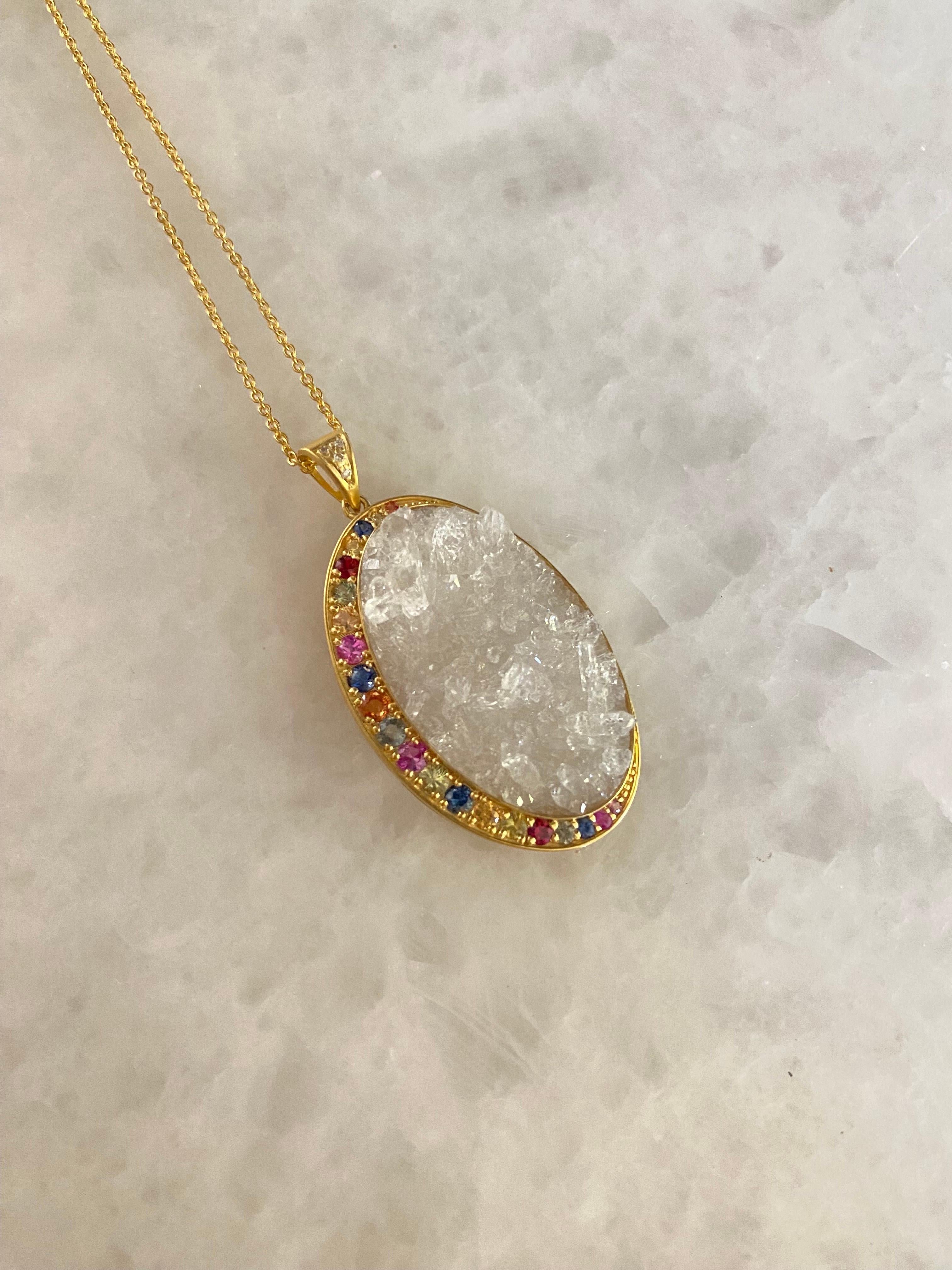 This stunning one of a kind Crystal Quartz center oval stone is three dimensional and incredibly eye catching. It is surrounded by a playful and colorful assortment of faceted round sapphires and is set in a custom warm tone alloy of 18kt gold.  The