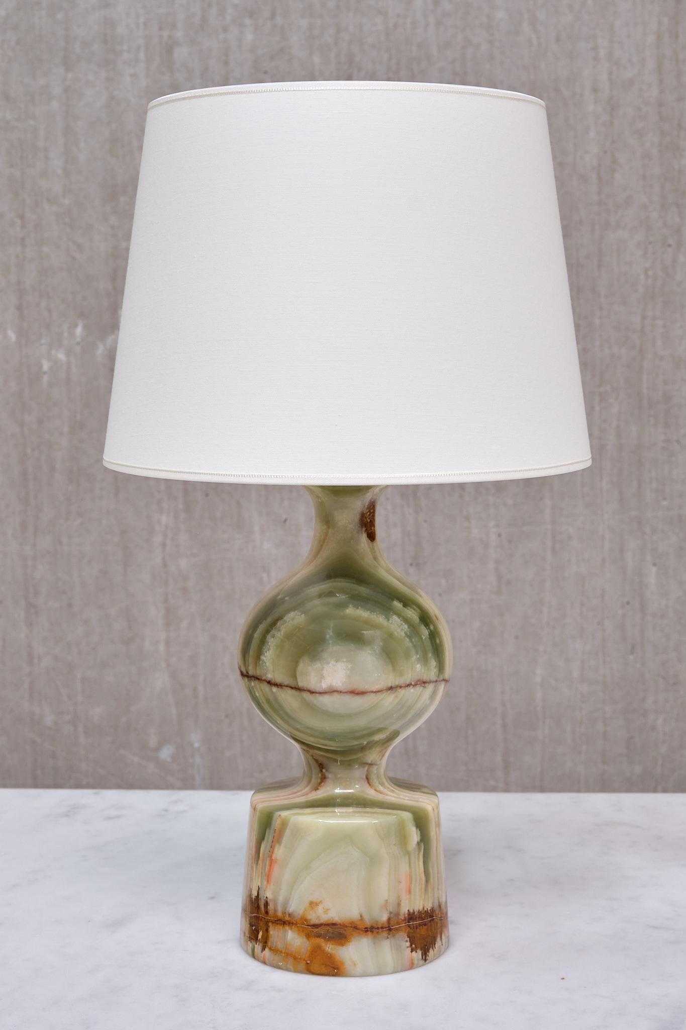 This elegant table lamp was crafted in Italy in the late 1970s. Its organic design features a central sphere resting atop a tapered base, both carved from the same single piece of solid onyx. The contrasting veins of green, brown, orange, and white