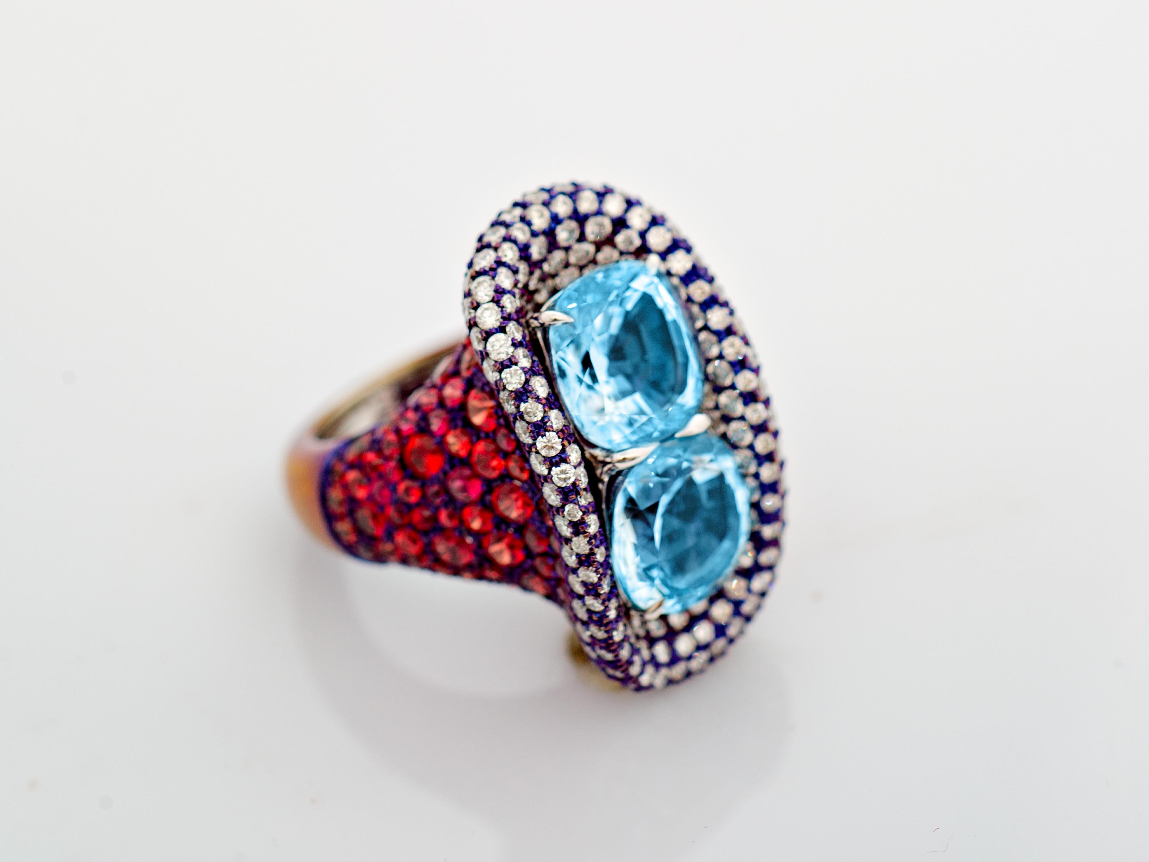 A carefully crafted titanium ring with two 10.27ct Blue Topaz stones set on the top, surrounded by 203 white diamonds along with 158 orange sapphires covering the lower aspect of the ring. A unique bold ring for a confident individual.